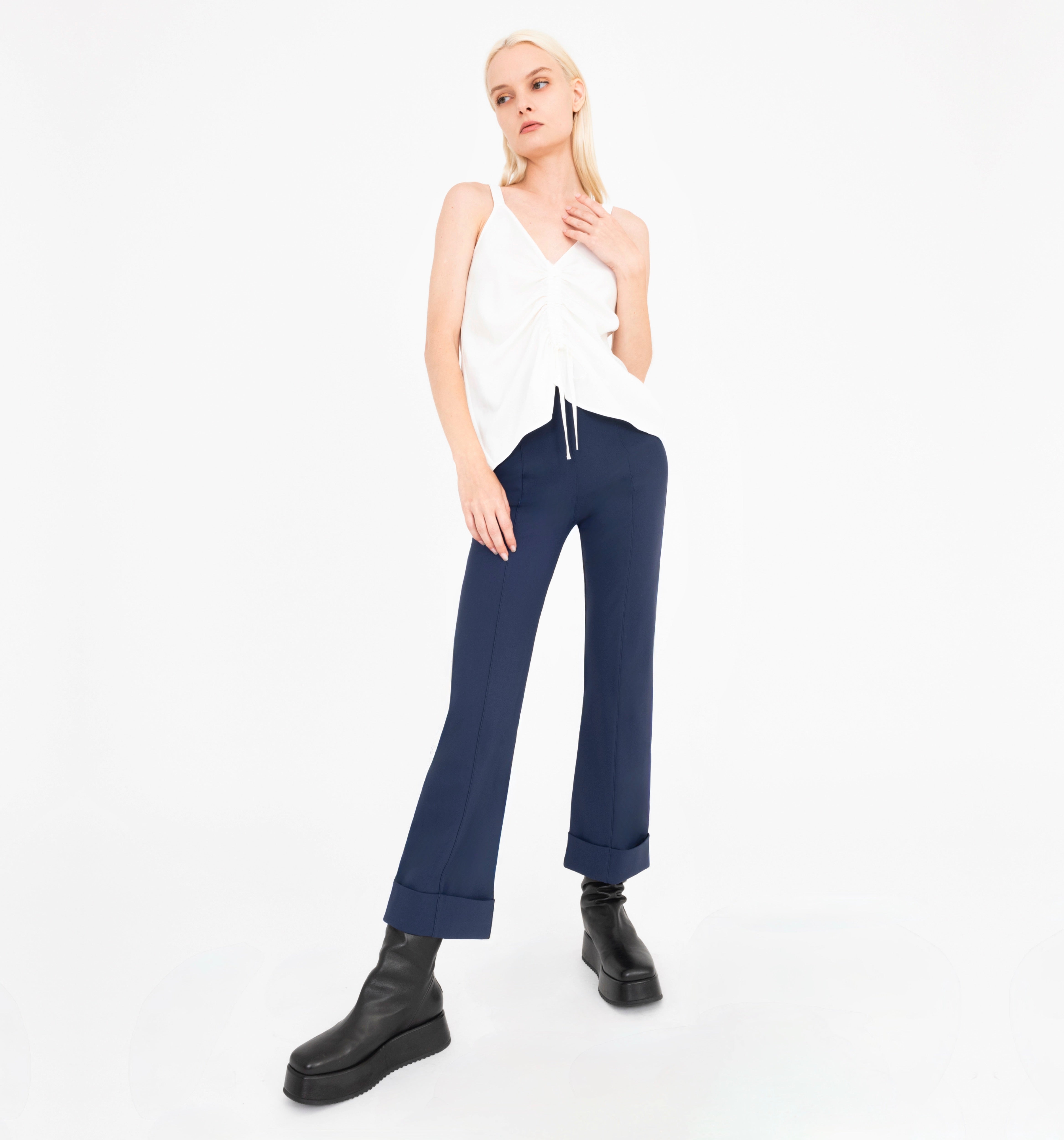 Woman wearing white sleeveless top and navy pants on a white background