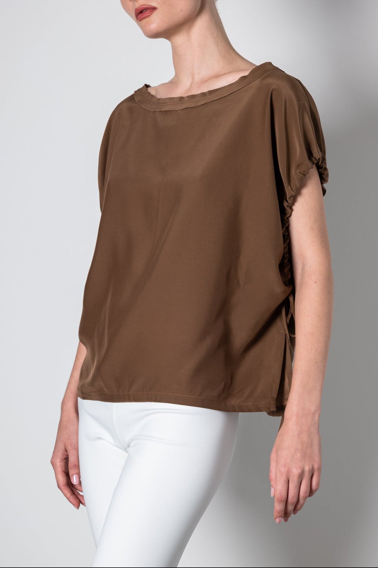 Woman wearing a brown blouse with ruffled sleeves on a plain background