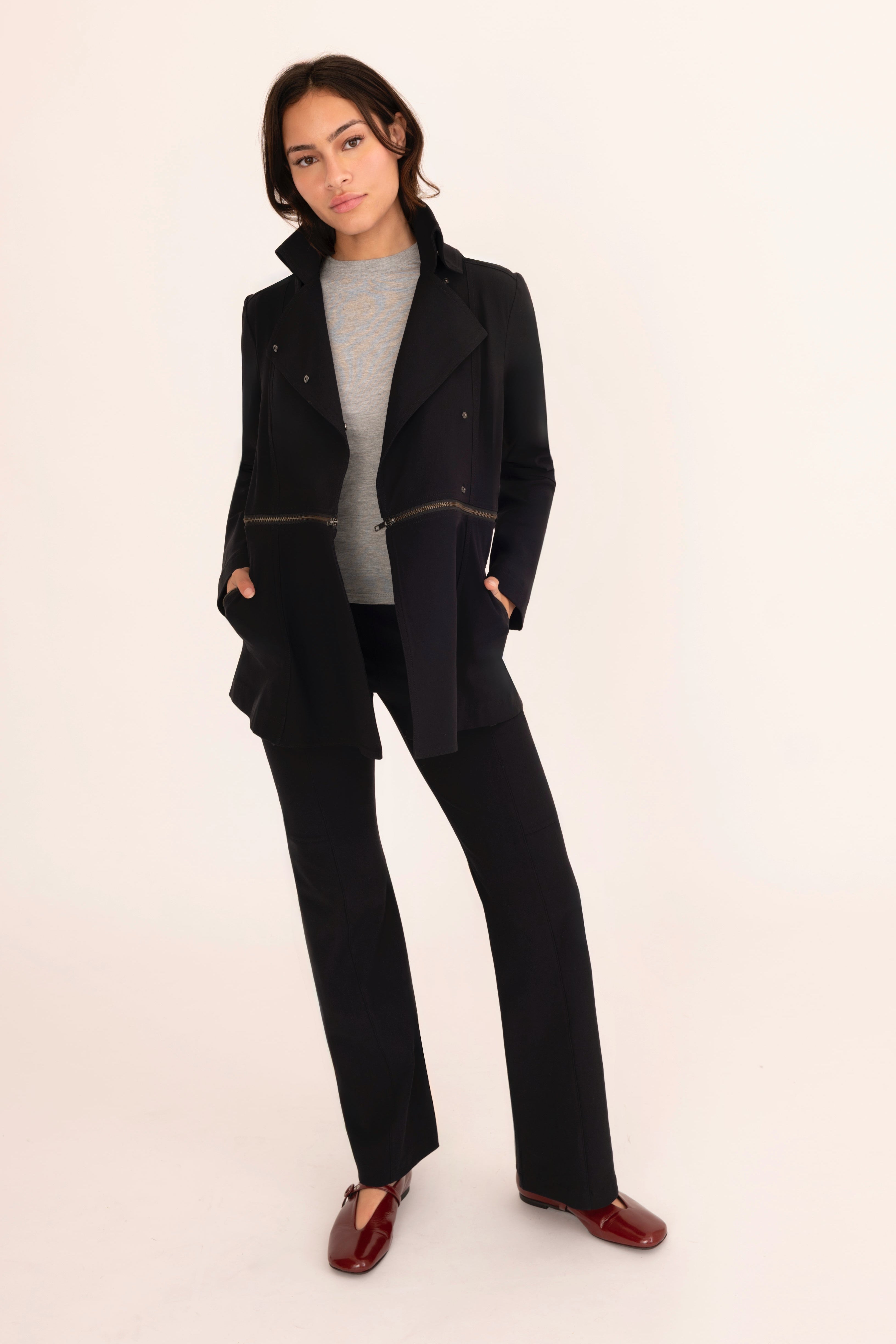 Woman wearing a black coat and pants with a gray top on a beige background