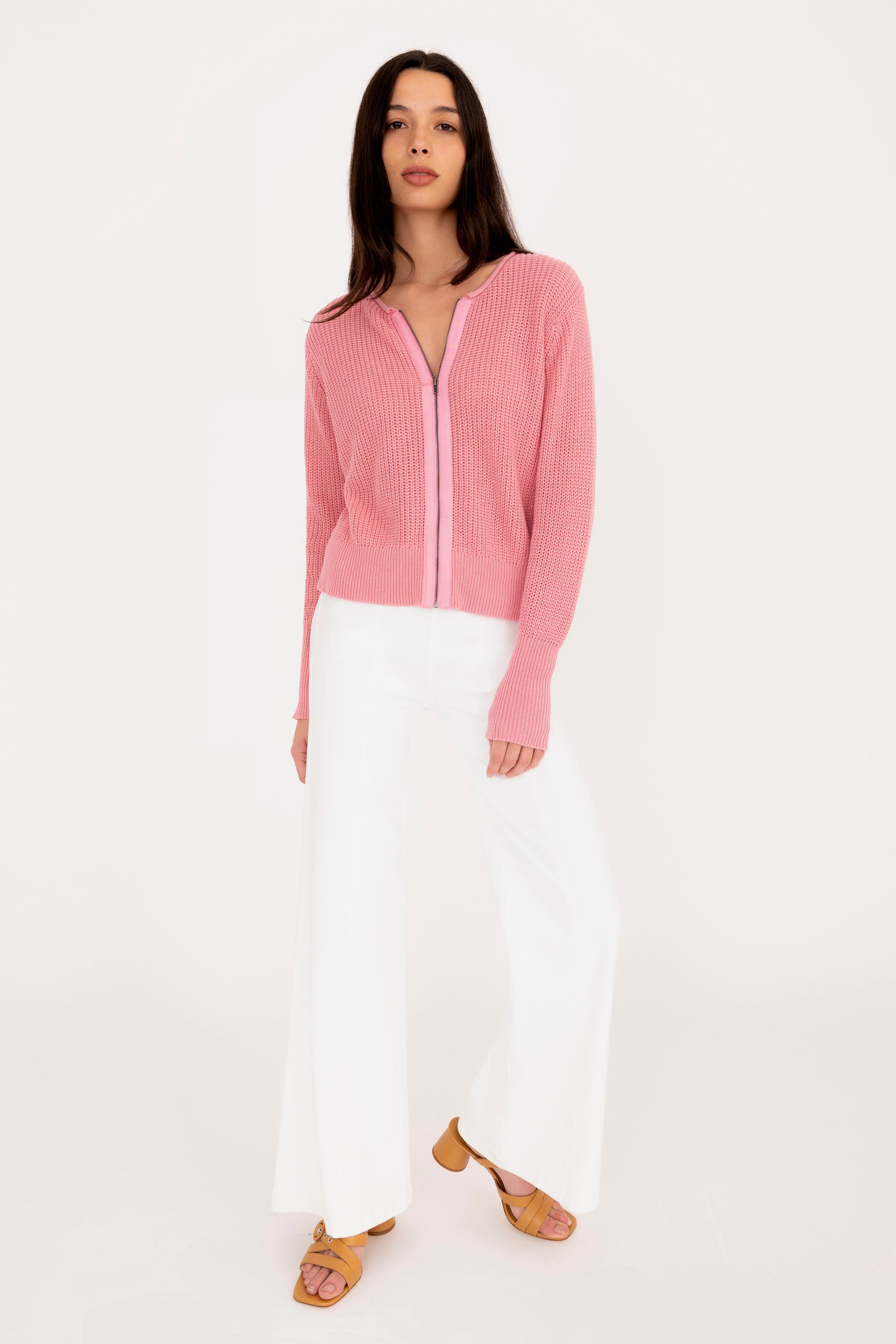 Woman wearing a pink zip-up top and white pants on a white background