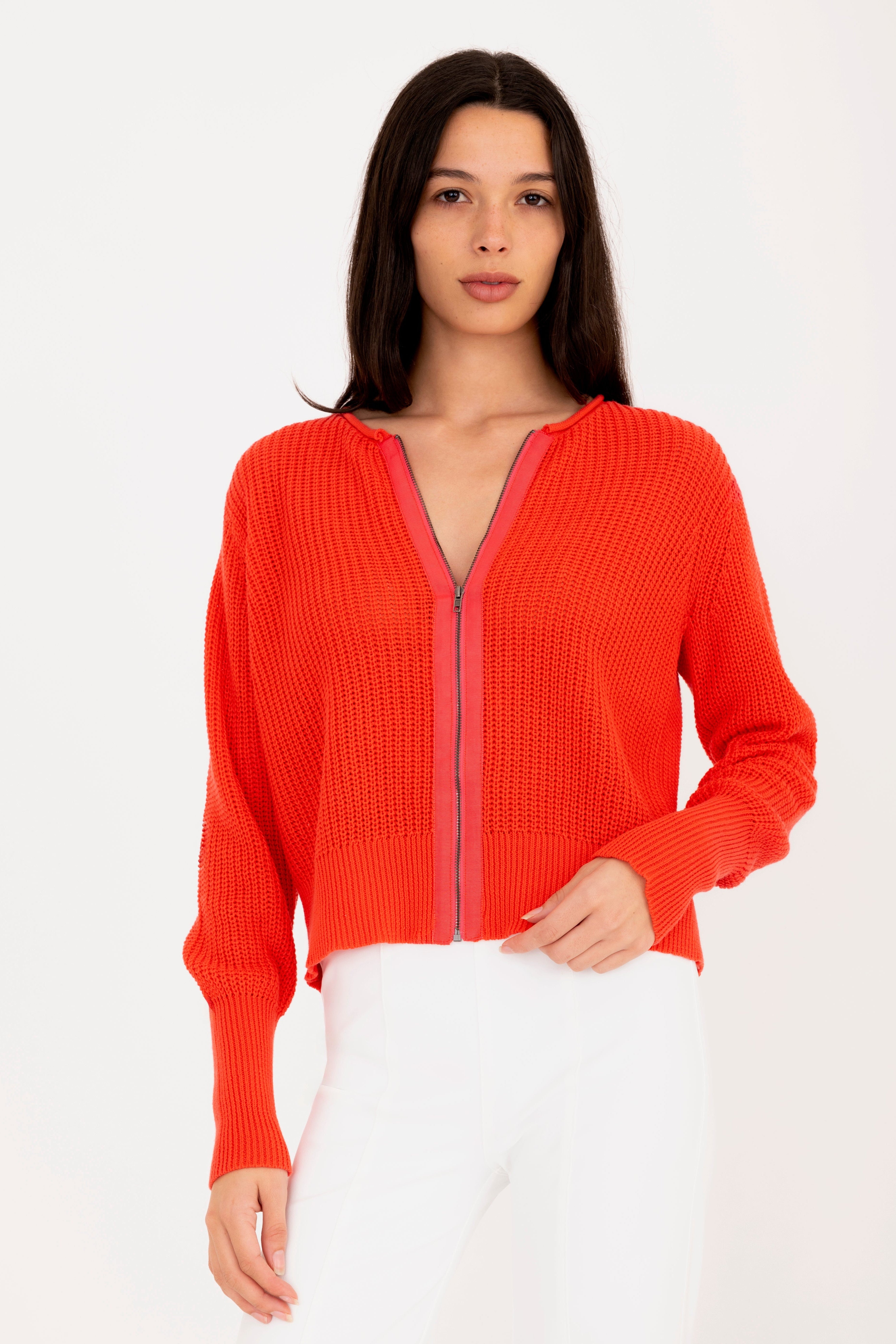 Woman wearing a orange zip-up sweater against a white background