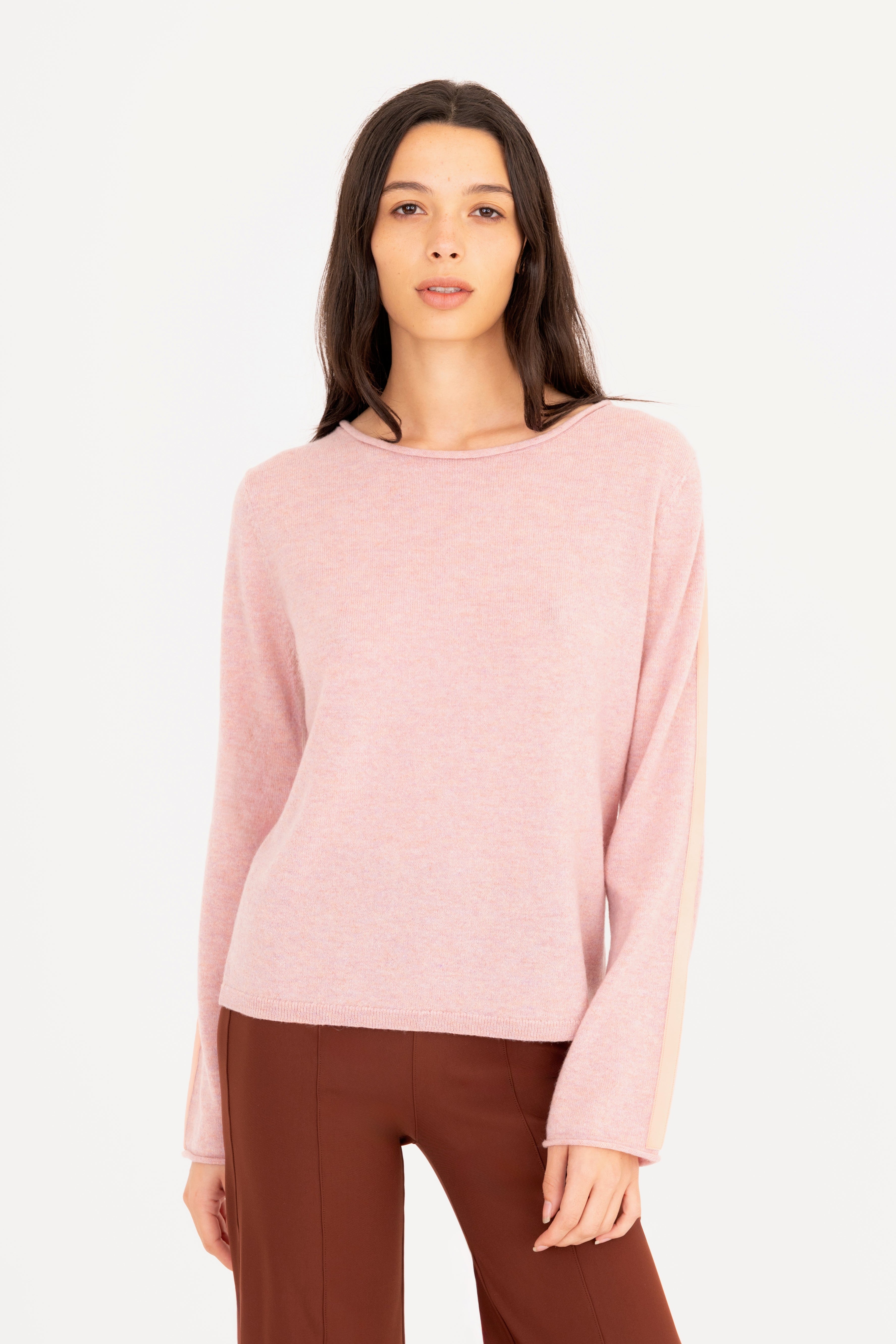 Woman wearing a pink sweater and brown pants on a white background