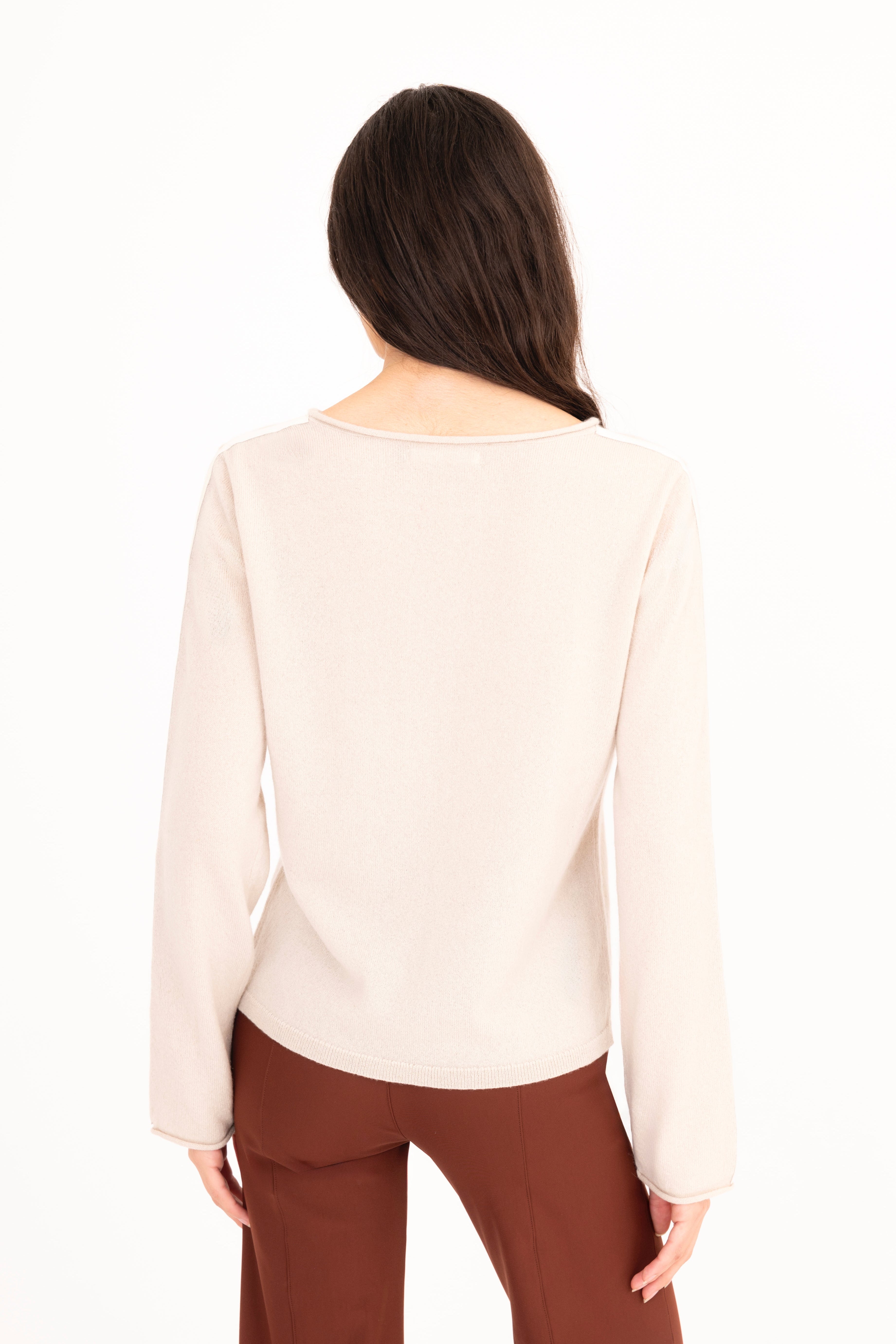 Woman wearing a beige long-sleeve top and brown pants on a white background