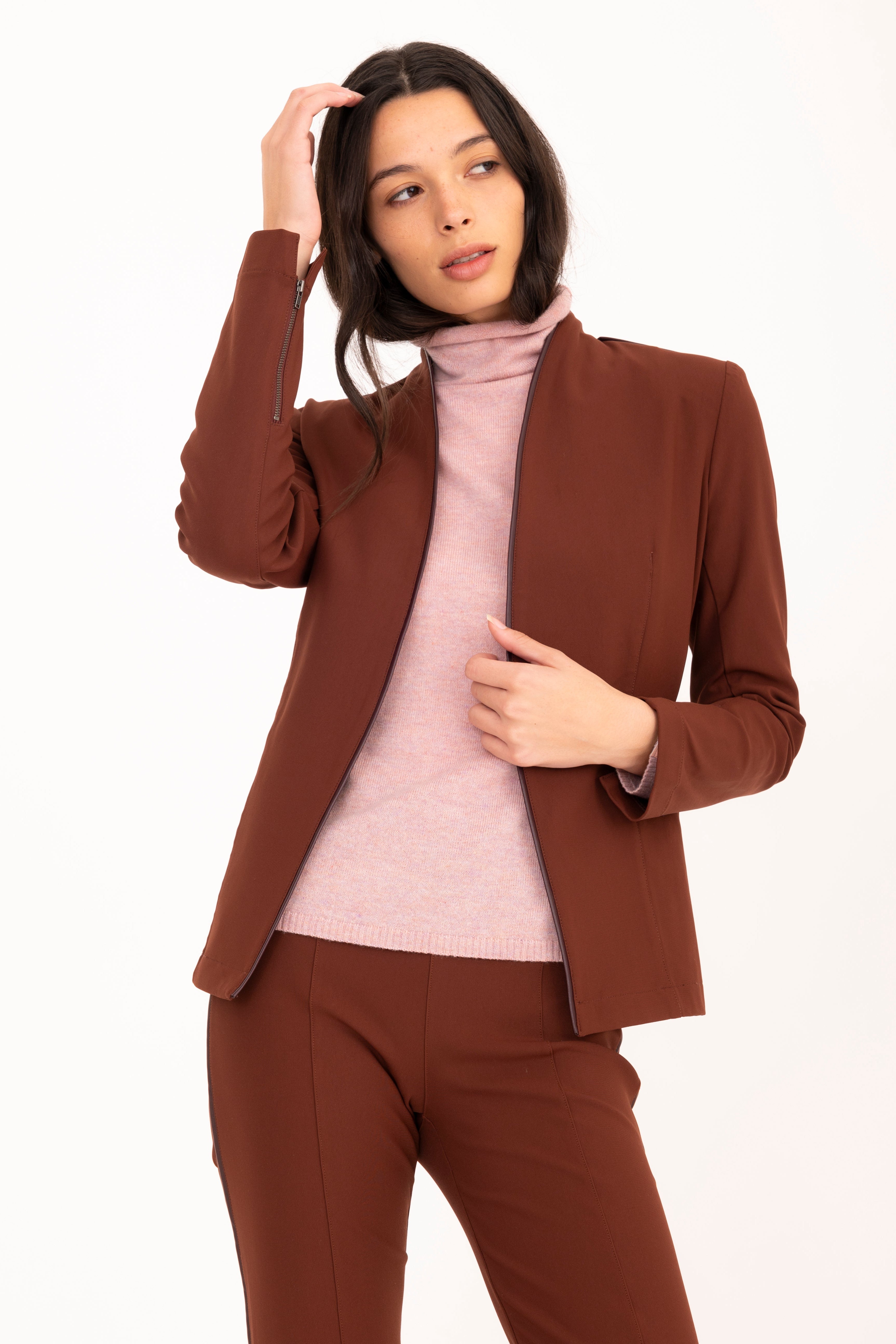 Woman wearing a brown suit with a pink turtleneck on a white background