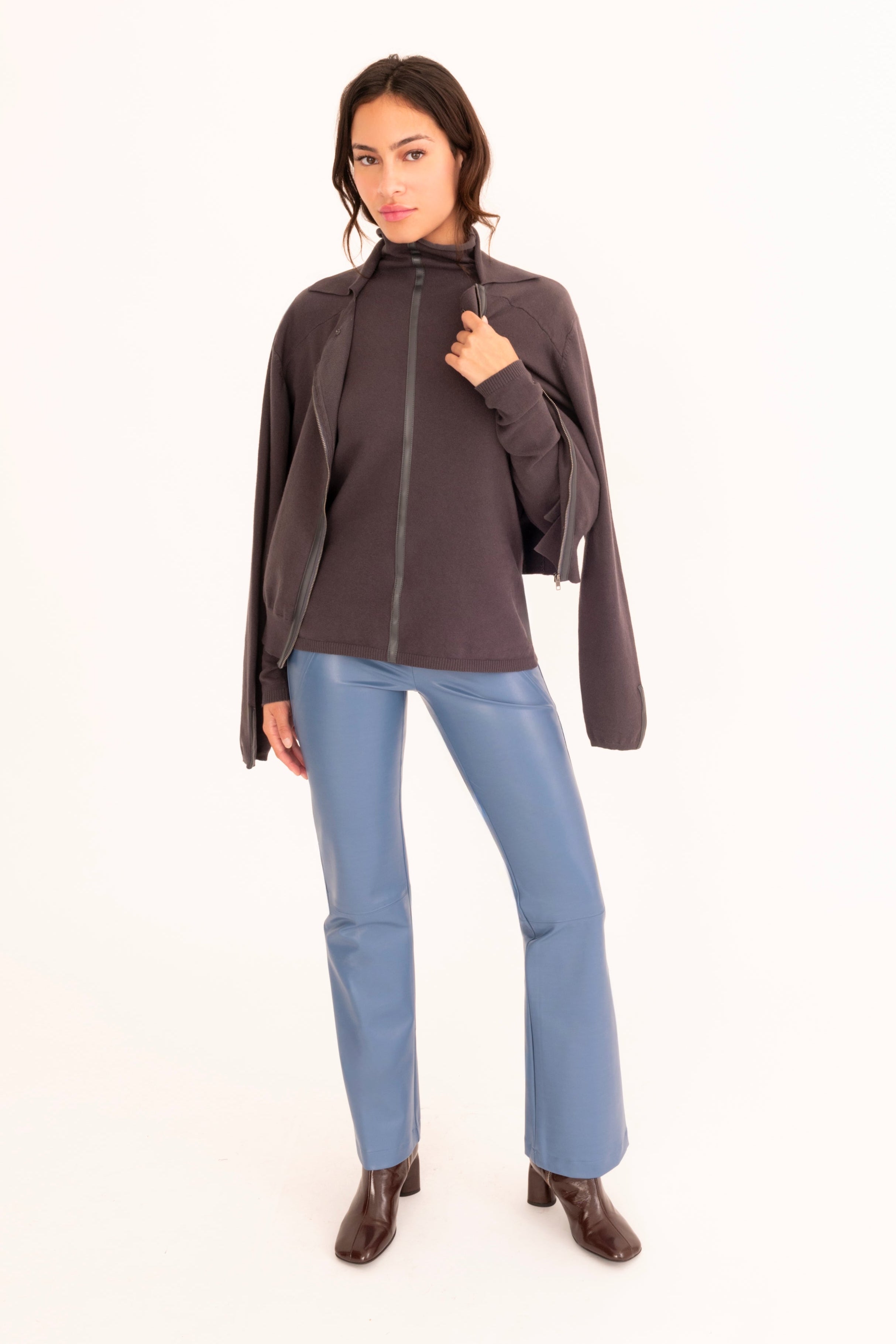 A woman modeling a gray zip-up jacket and light blue faux-leather pants against a plain white studio background.