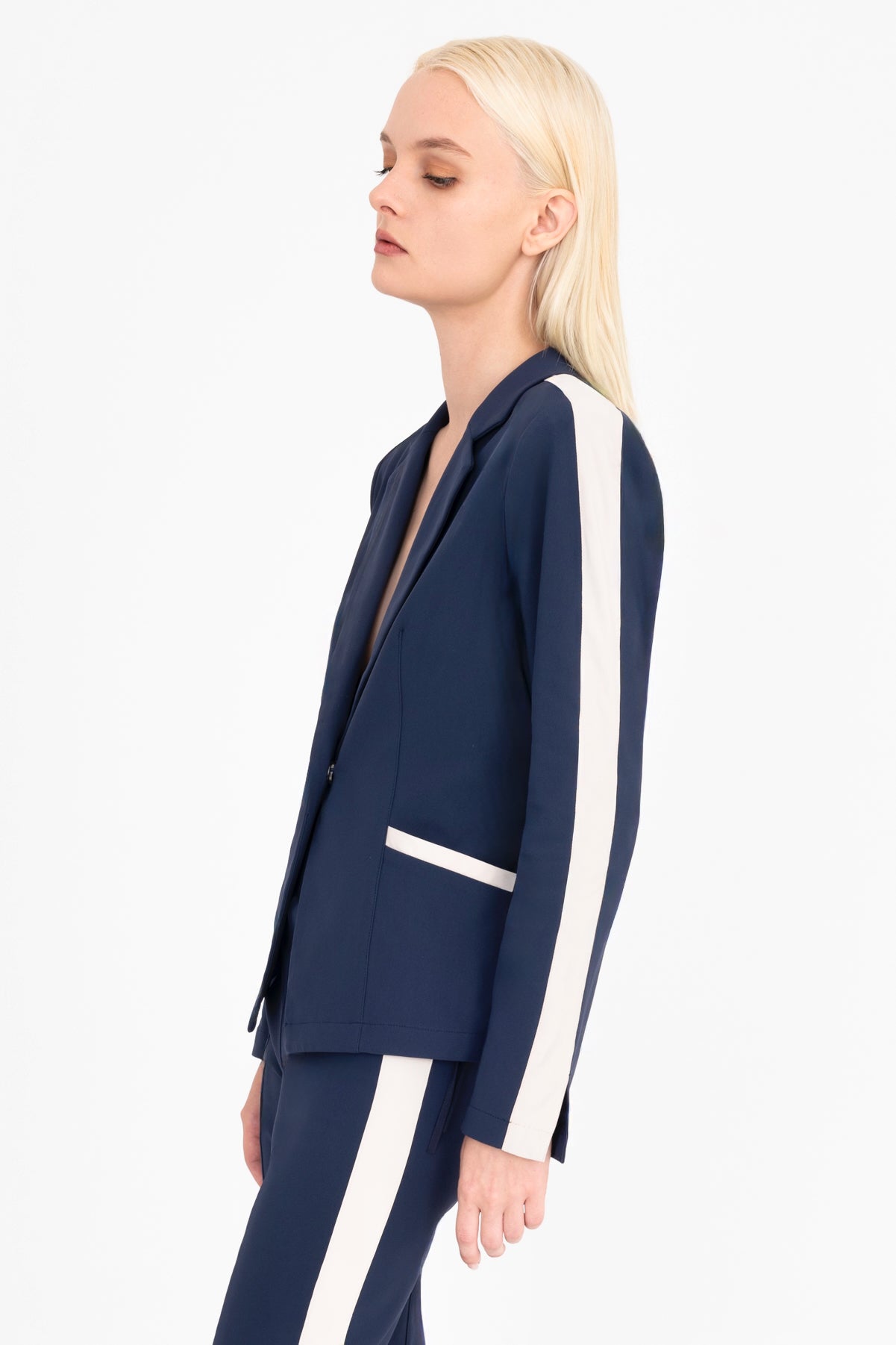 Woman wearing a indigo blue blazer with beige side stripe on a white background