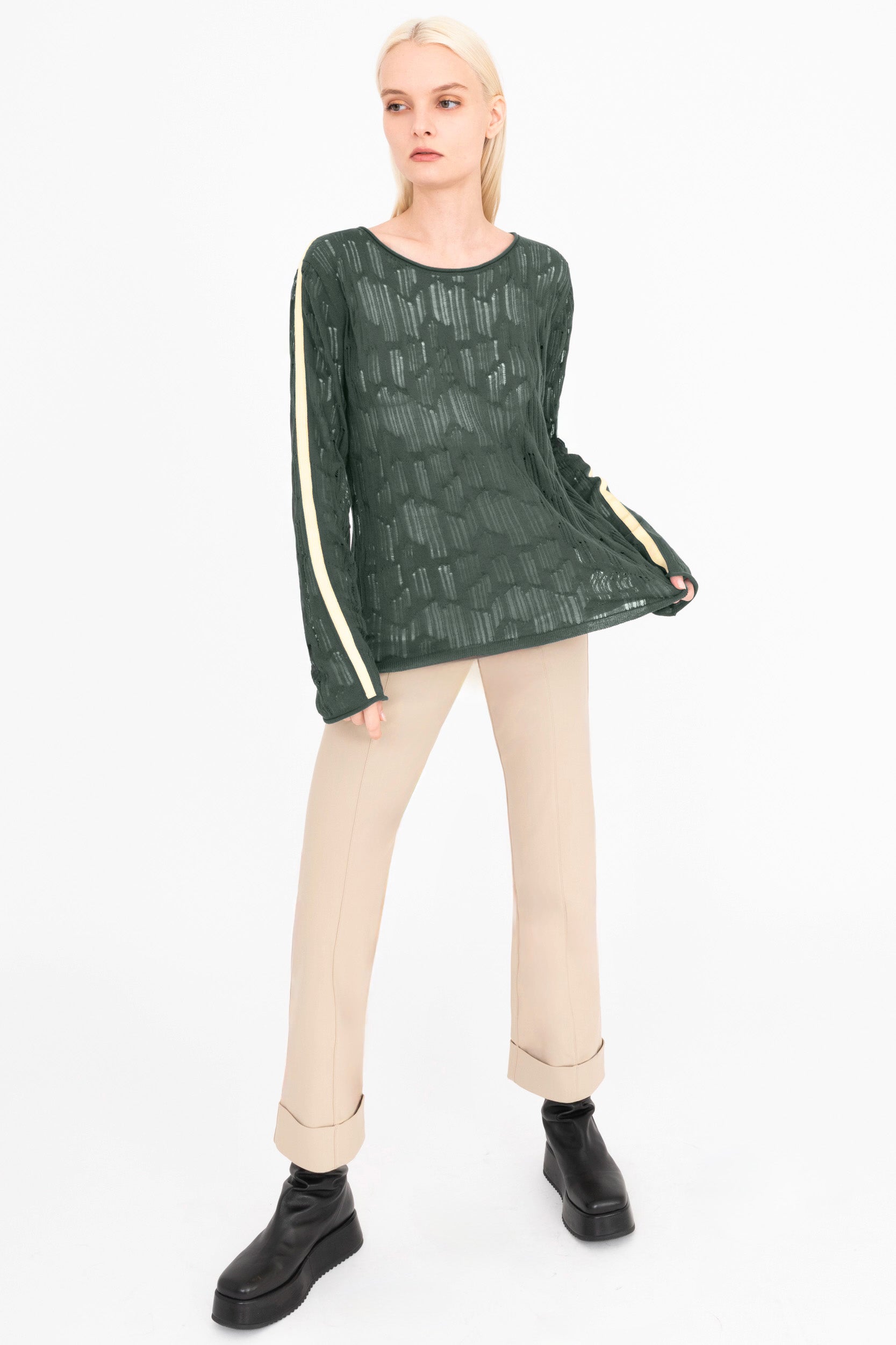 Woman wearing a green sheer top with cream stripes and beige pants on a white background