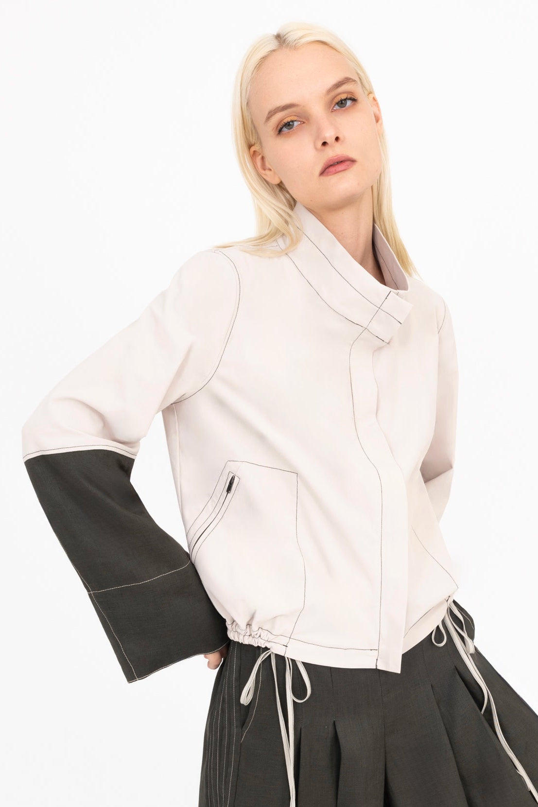 Woman wearing a beige and pine green jacket with a white background
