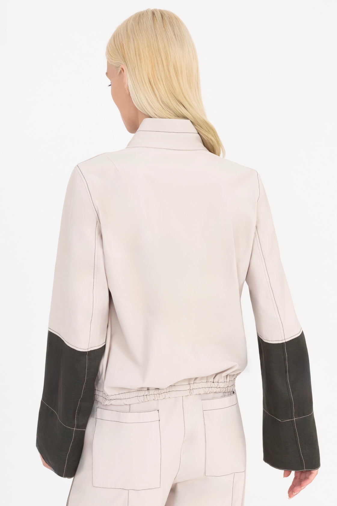 Woman wearing a beige and pine green jacket with a white background