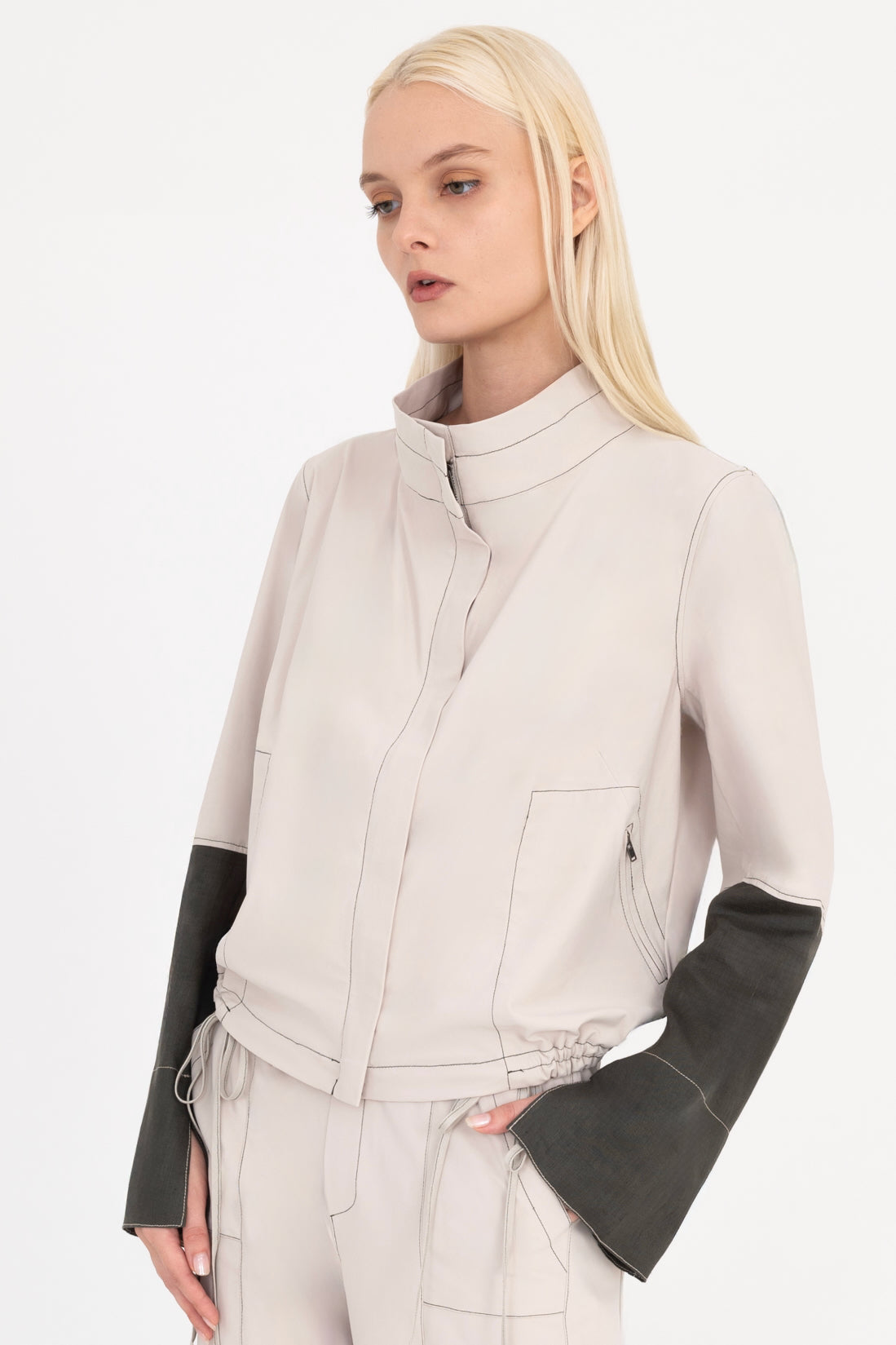 Woman wearing a beige and pine green jacket with a white background
