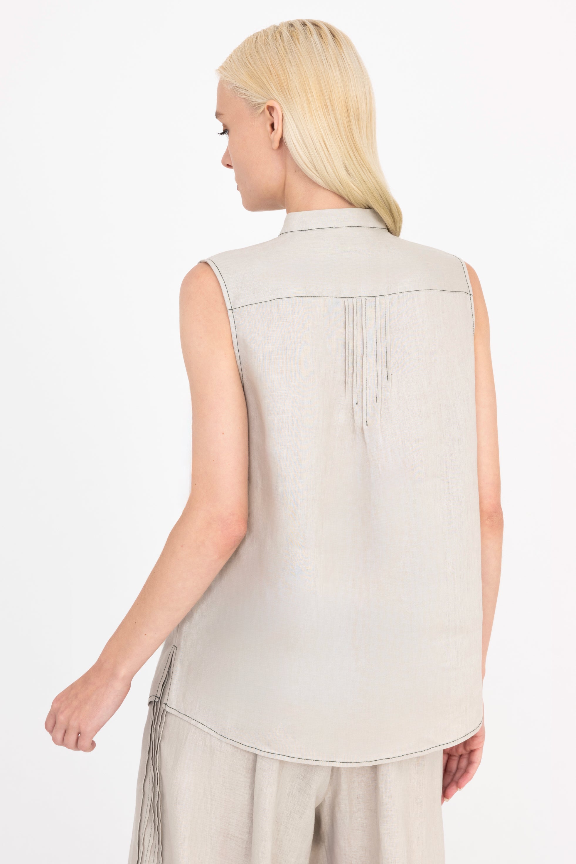 Woman wearing a beige sleeveless top with a plain background