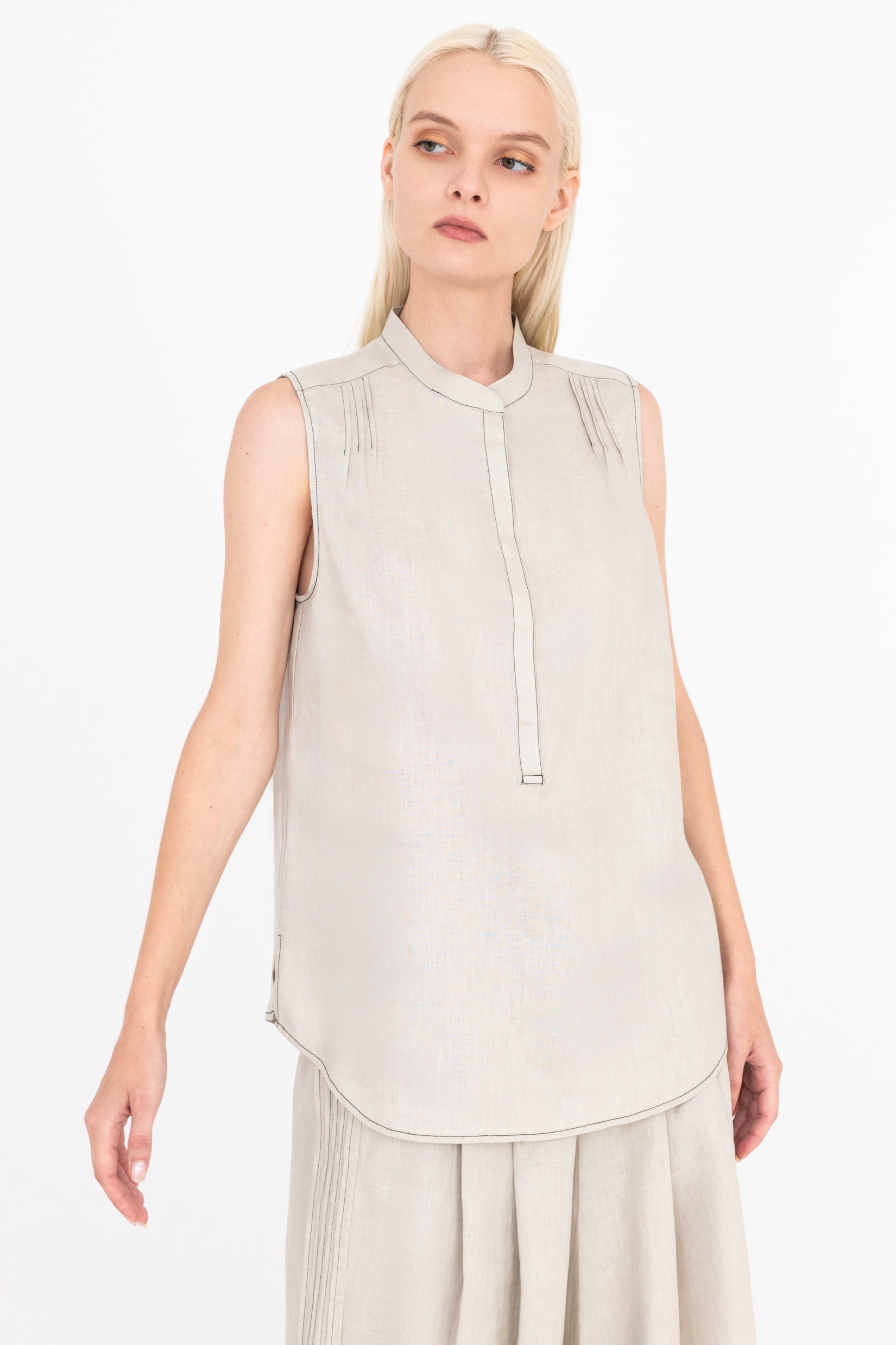 Woman wearing a beige sleeveless top with a high collar on a white background