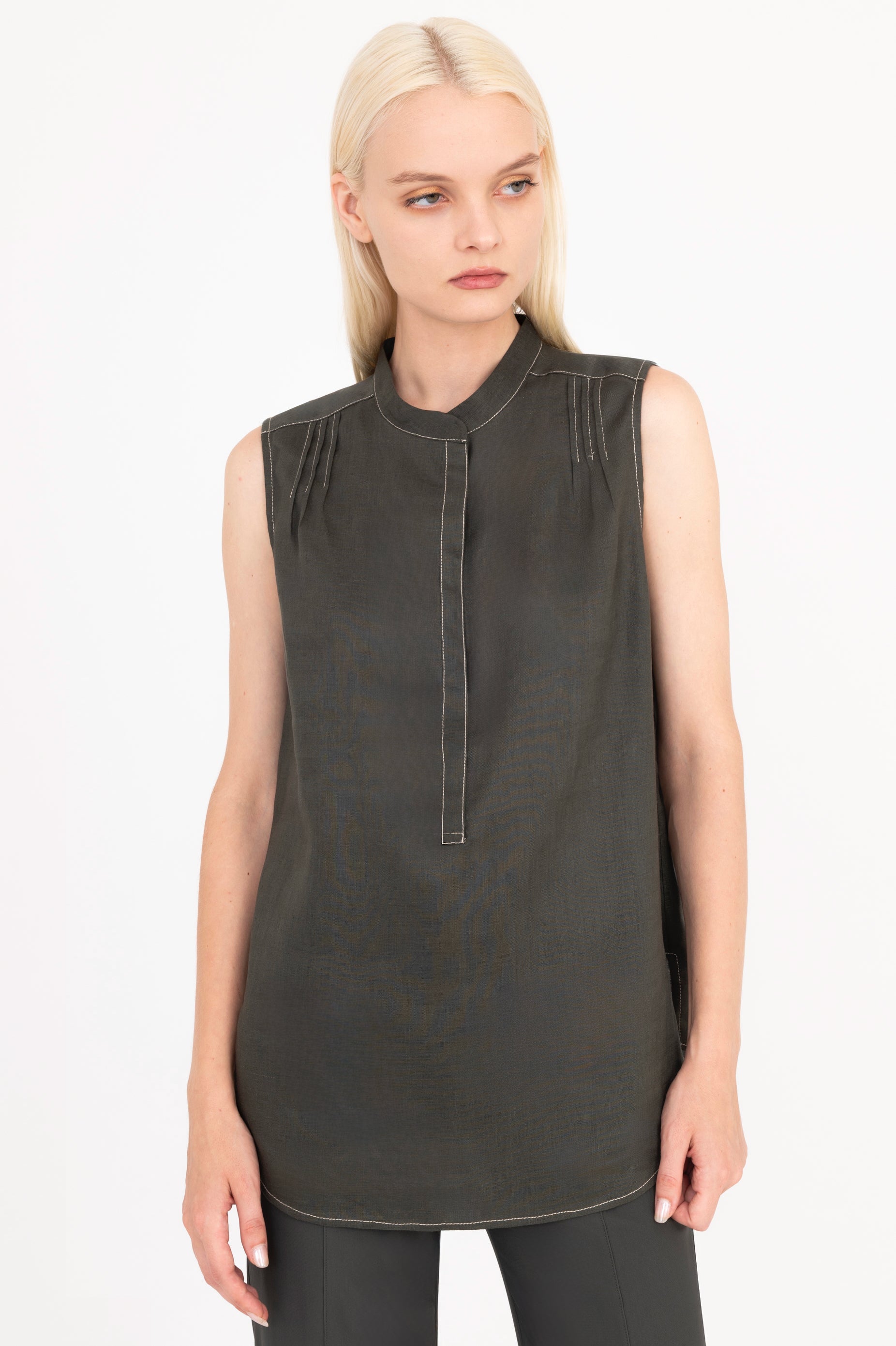 Woman wearing a sleeveless dark green top with a high neckline on a white background