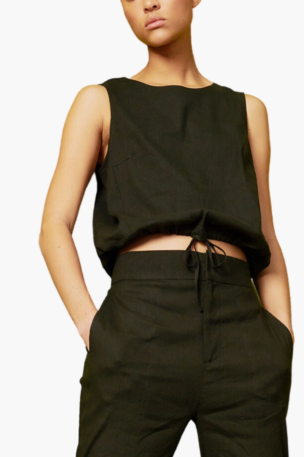 Person wearing a black sleeveless top and dark pants on a white background
