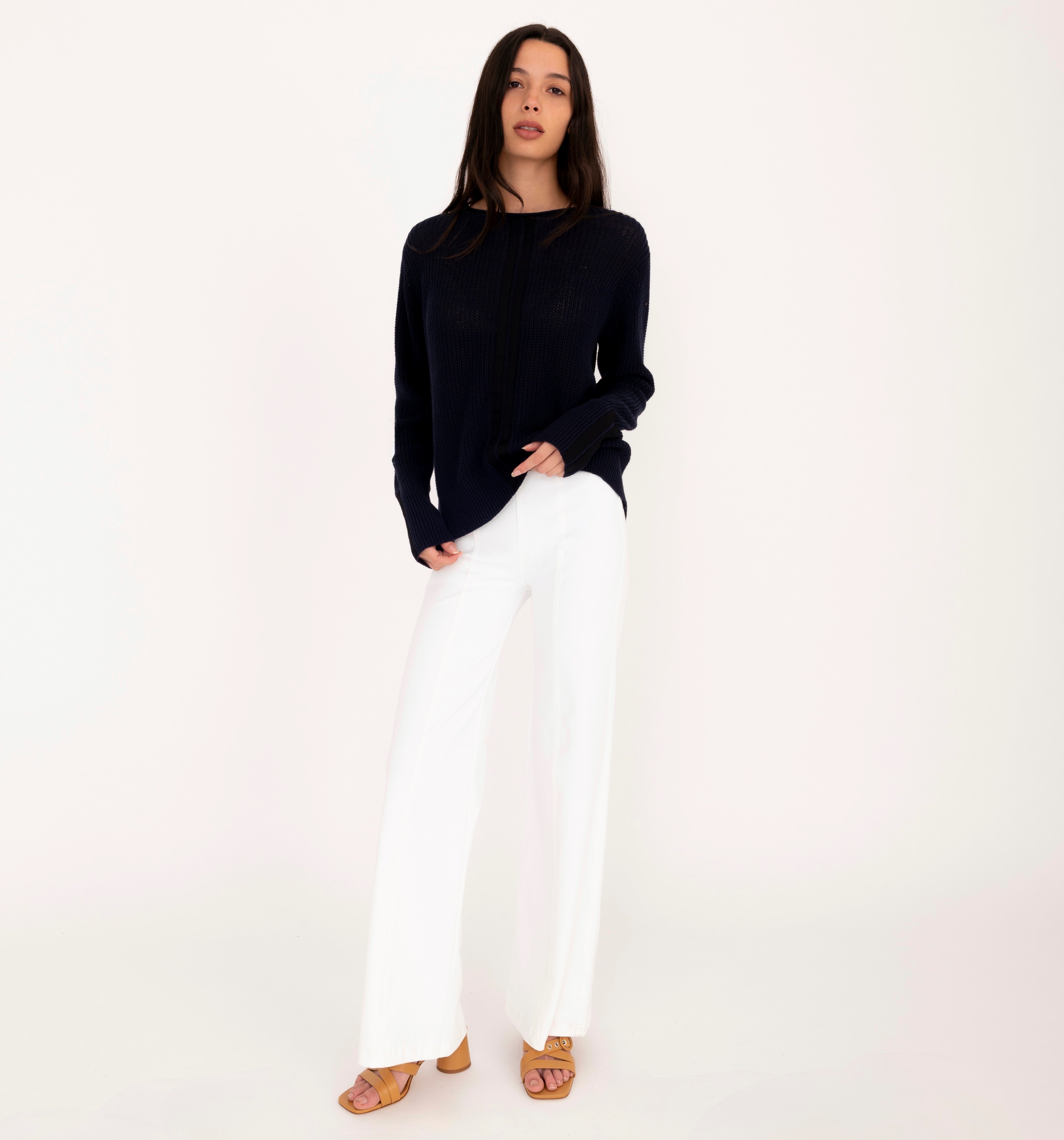 Woman wearing a black sweater and white pants on a white background