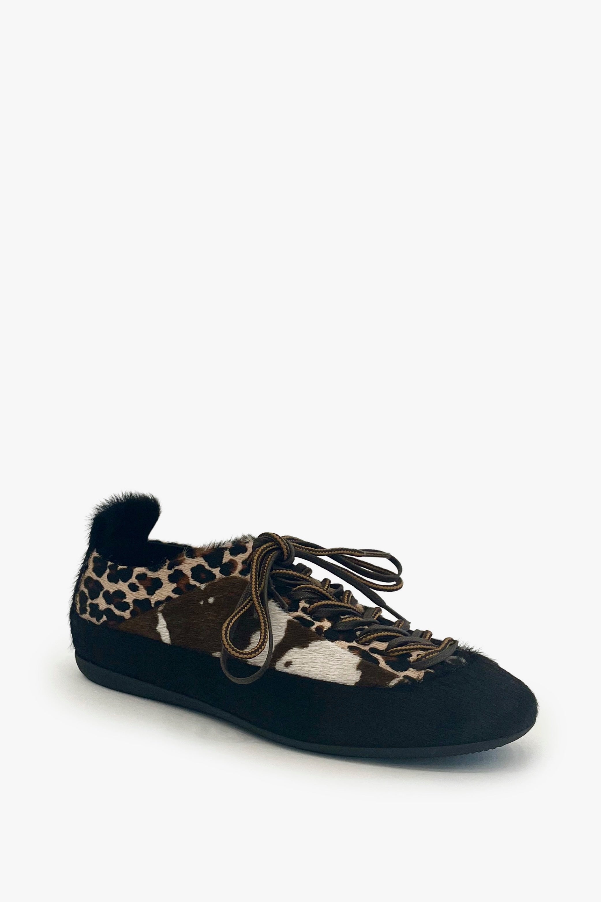 A single slip-on shoe with a black suede-like sole and heel, a fuzzy black fur collar, and a leopard print upper. The leopard pattern features brown, black, and beige tones, and the shoe is shown from a three-quarters angle on a light gray background.