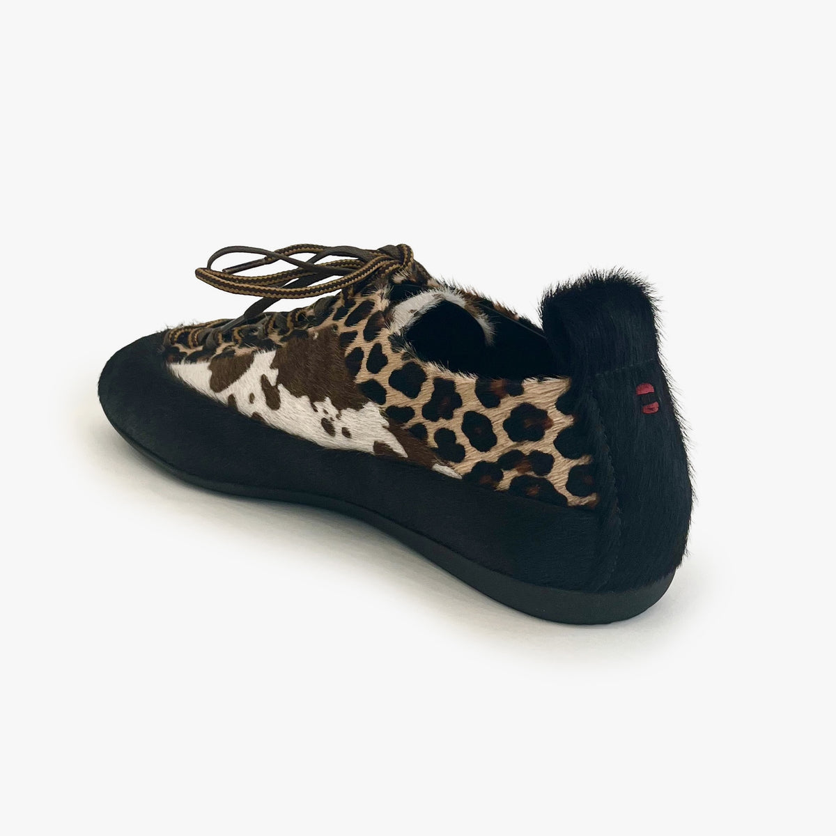 A single slip-on shoe with a black suede-like sole and heel, a fuzzy black collar, and a leopard print upper. The leopard pattern features brown, black, and beige tones, and the shoe is shown from a three-quarters angle on a light gray background.