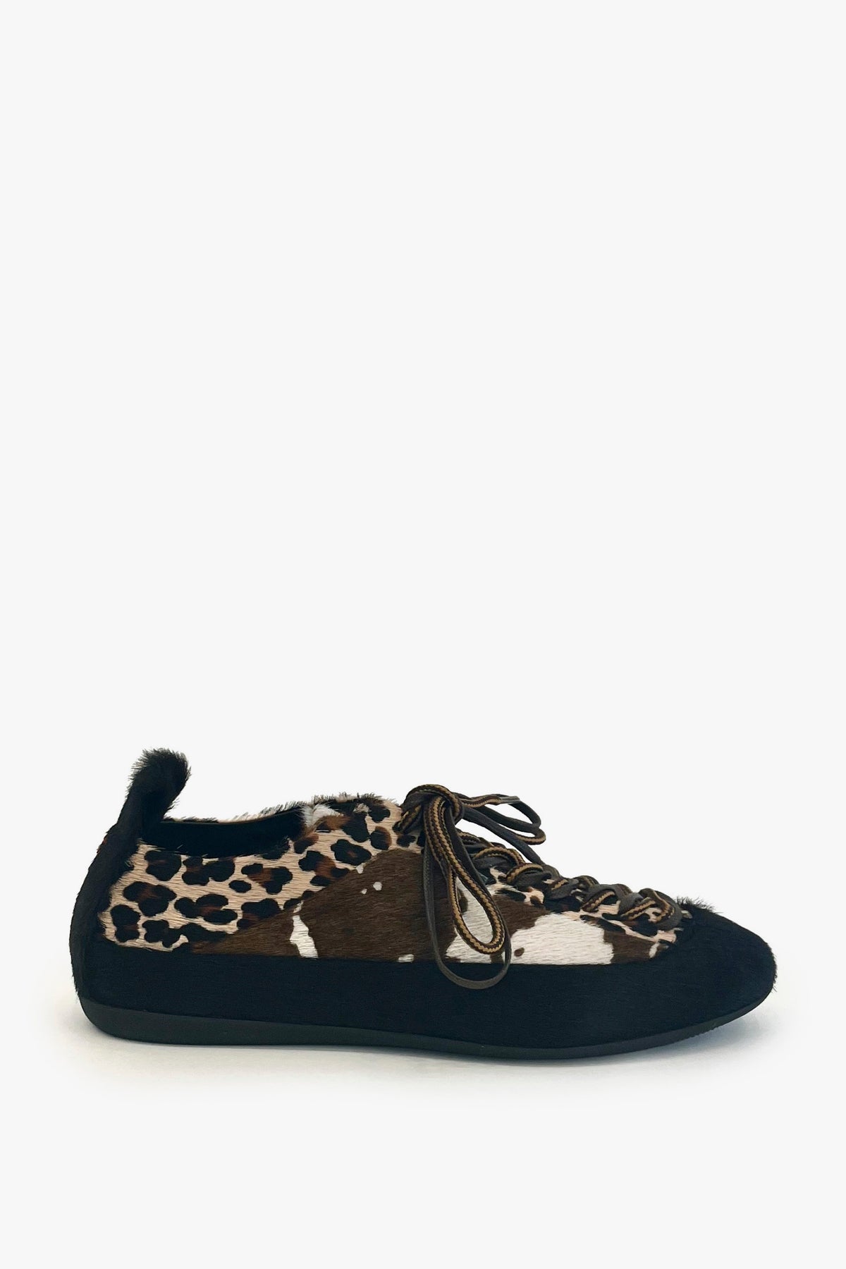 A single slip-on shoe with a black suede-like sole and heel, a fuzzy black fur collar, and a leopard print upper. The leopard pattern features brown, black, and beige tones, and the shoe is shown from a three-quarters angle on a light gray background.