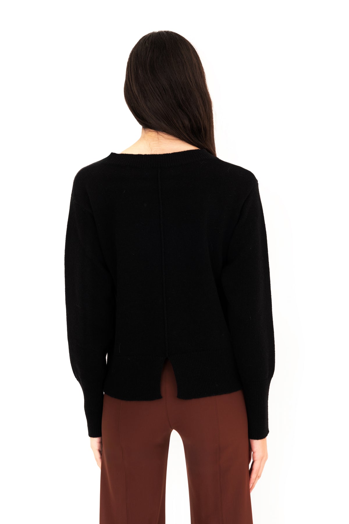 A woman viewed from the back wearing a black long-sleeve knit top and brown pants against a plain white background.