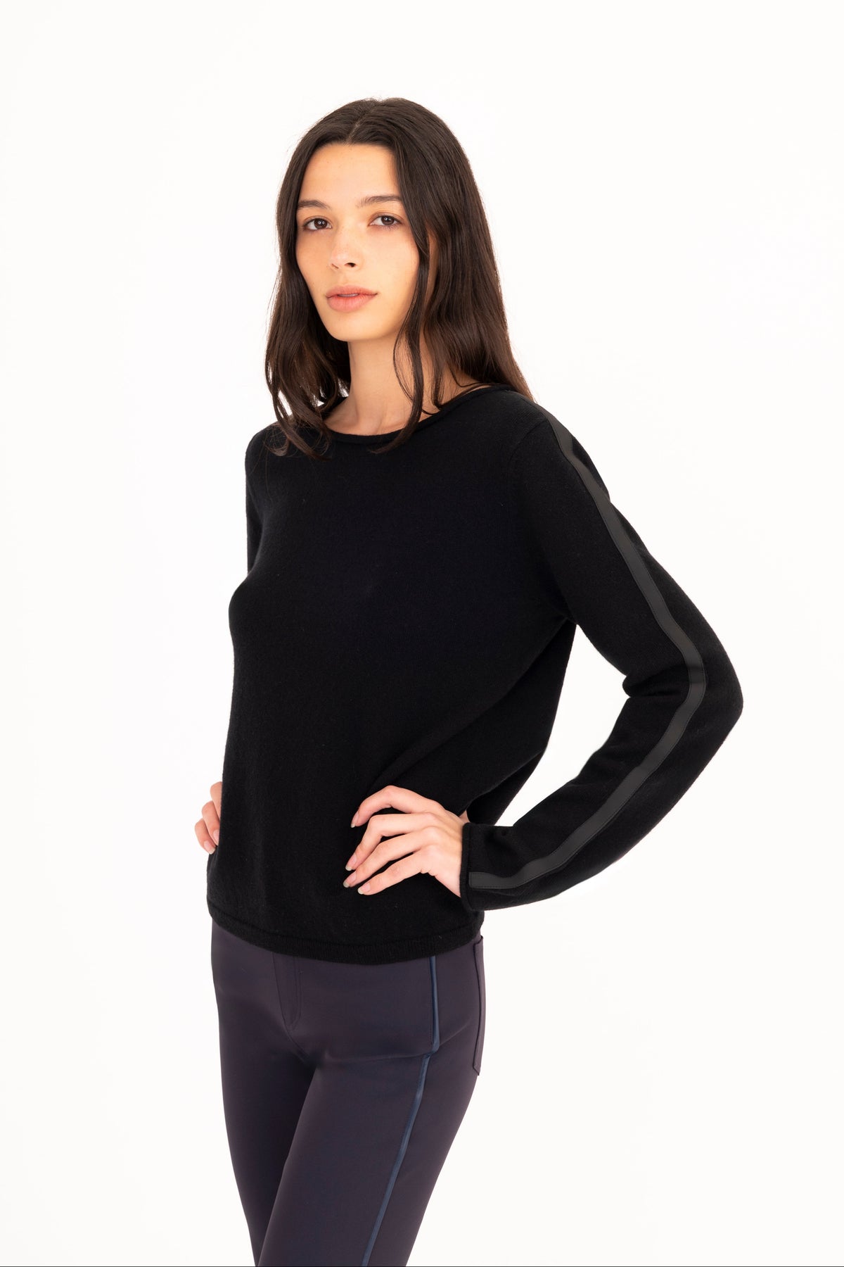 A woman modeling a black long-sleeve knit sweater, paired with navy blue pants, against a plain white studio background.
