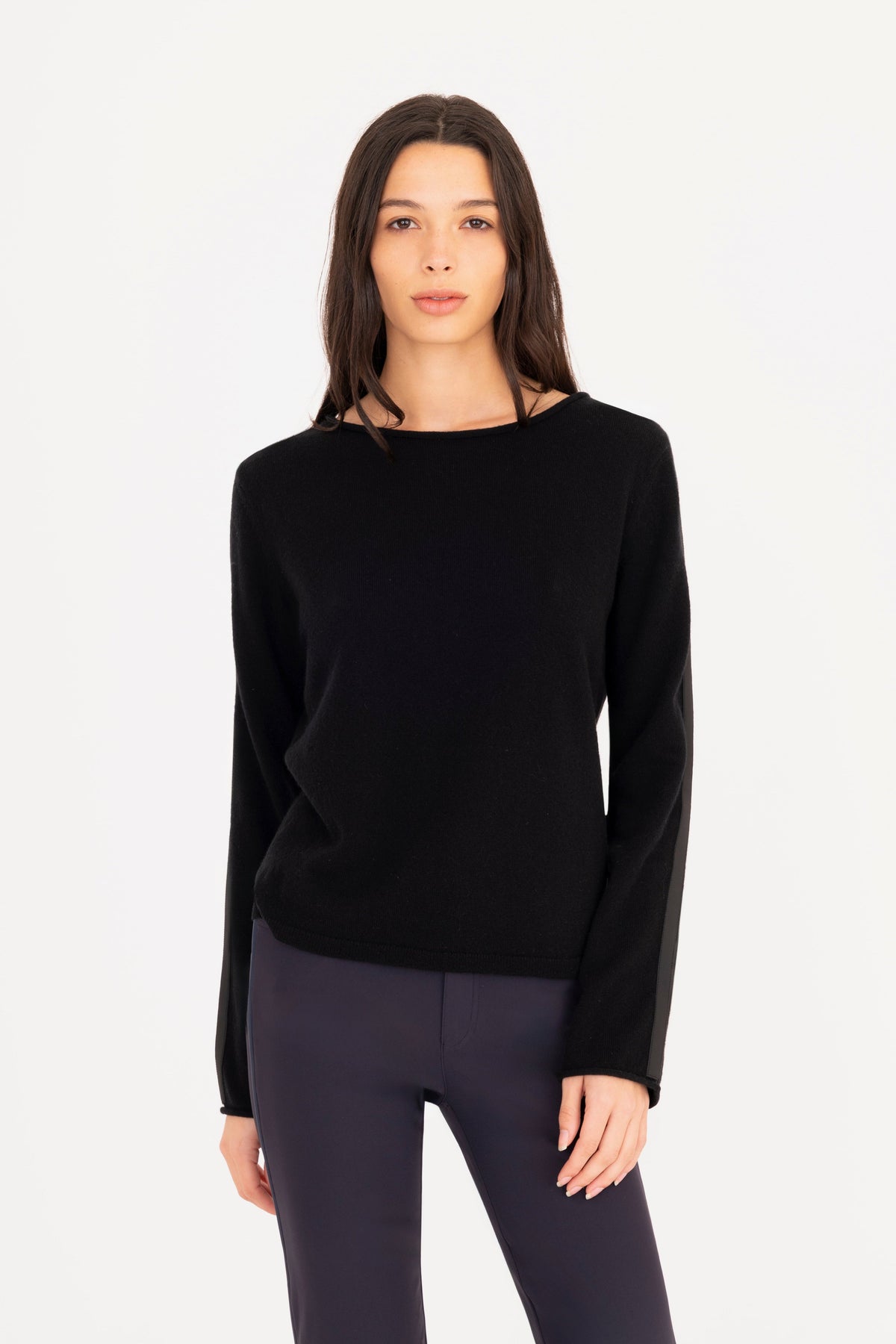 A woman modeling a black long-sleeve knit sweater, paired with navy blue pants, against a plain white studio background.
