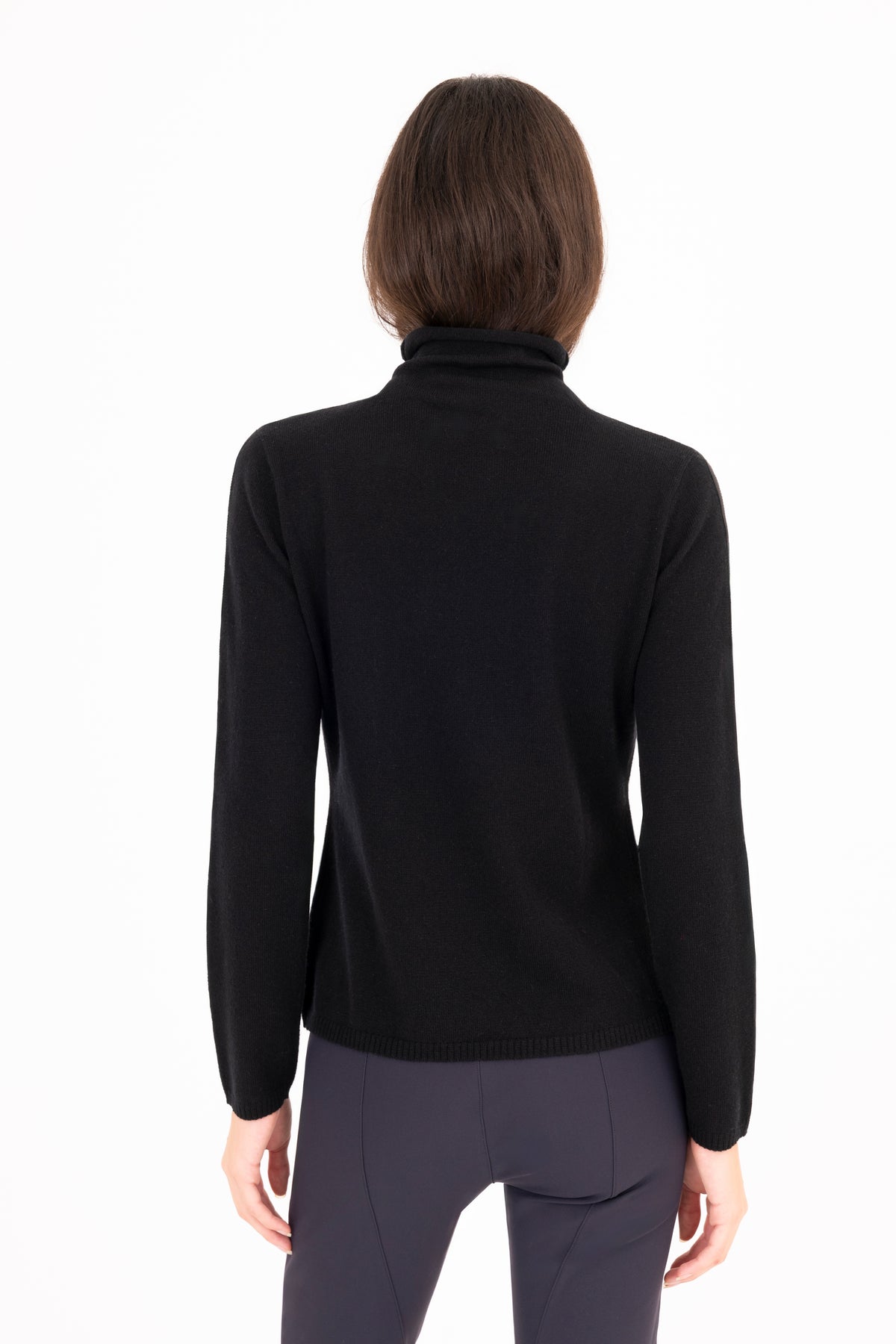 A woman viewed from the back wearing a black long-sleeve mock neck sweater and dark navy pants against a plain white background.