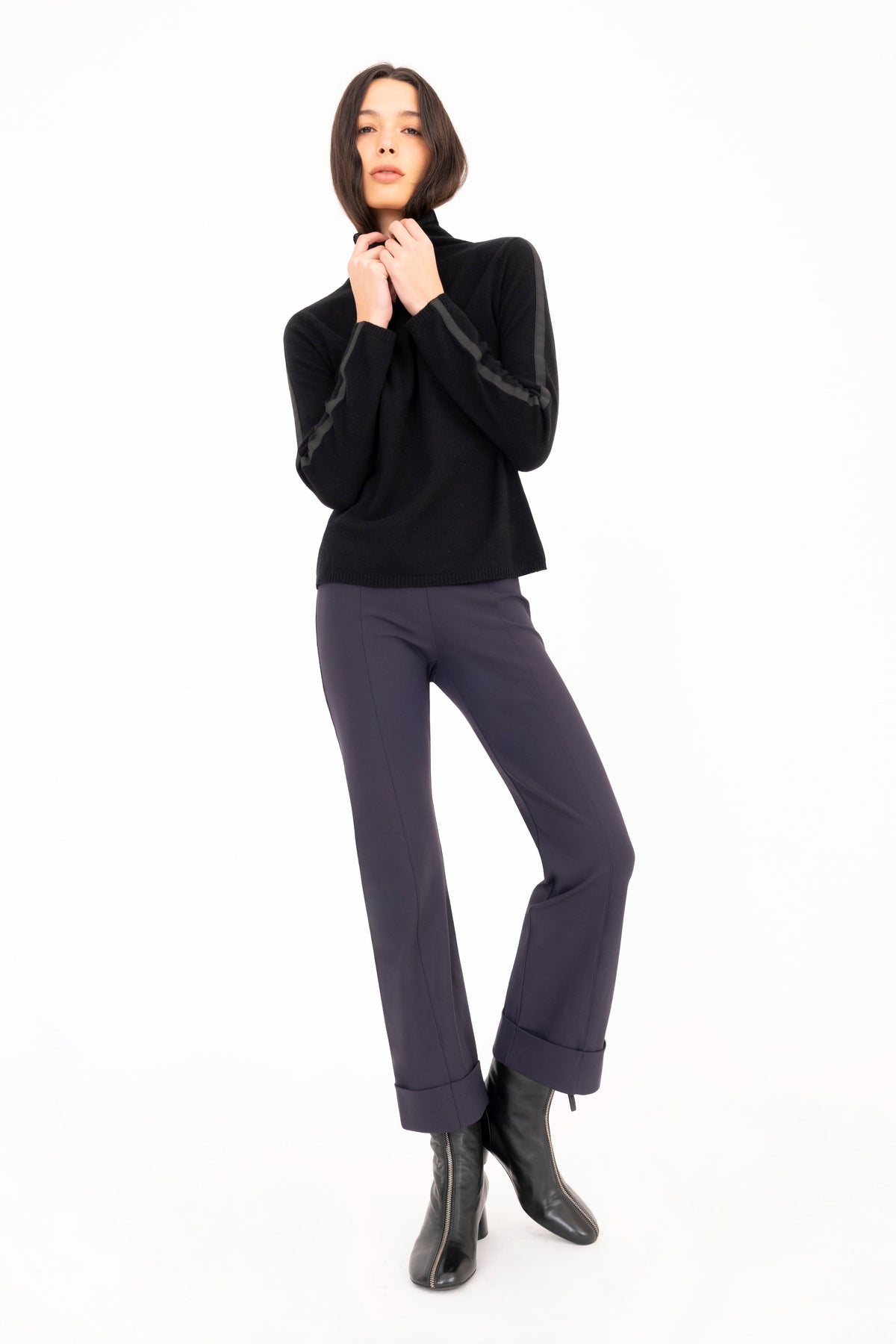 A woman modeling a black long-sleeve mock neck knit sweater, paired with dark navy pants against a plain white studio background.