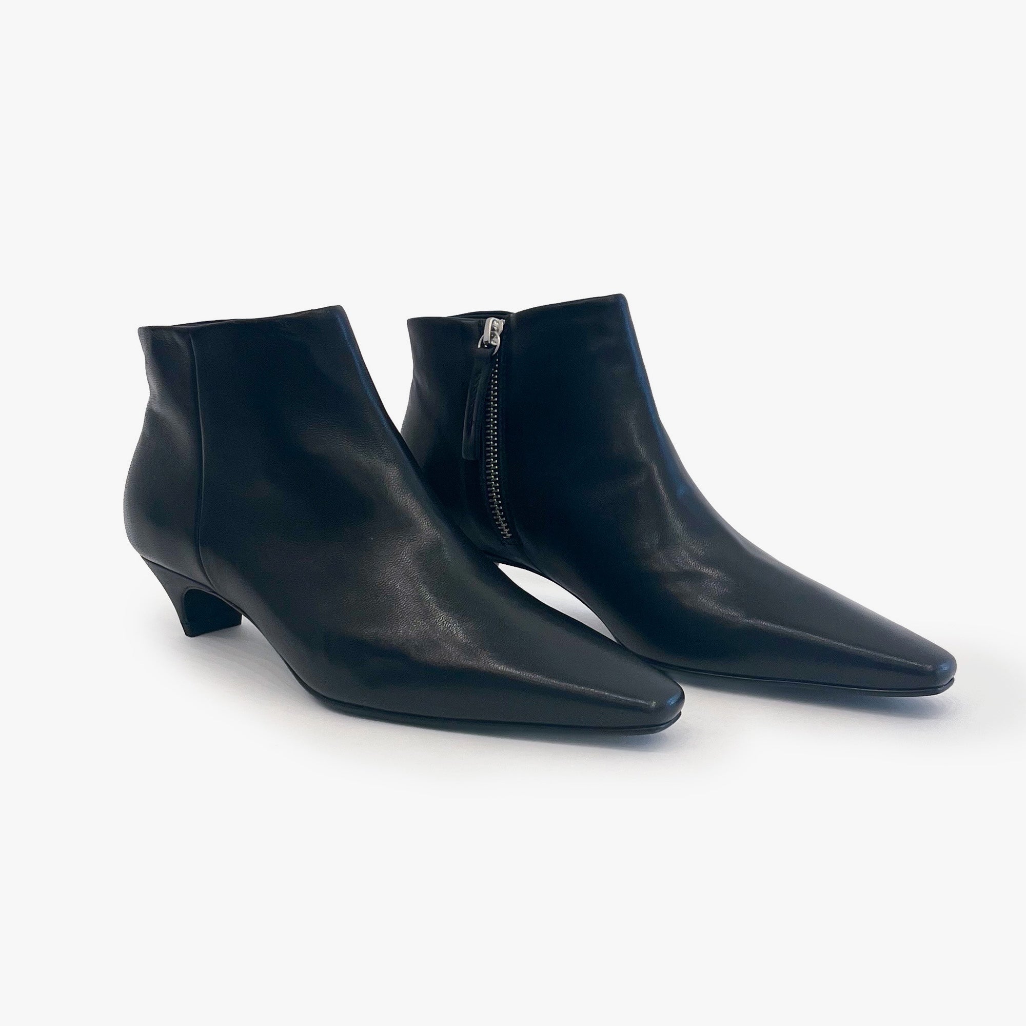 A pair of black leather ankle boots with pointed toes and low kitten heels, shown on a clean white background. One boot is positioned in front of the other, showing a side zipper on the rear boot.