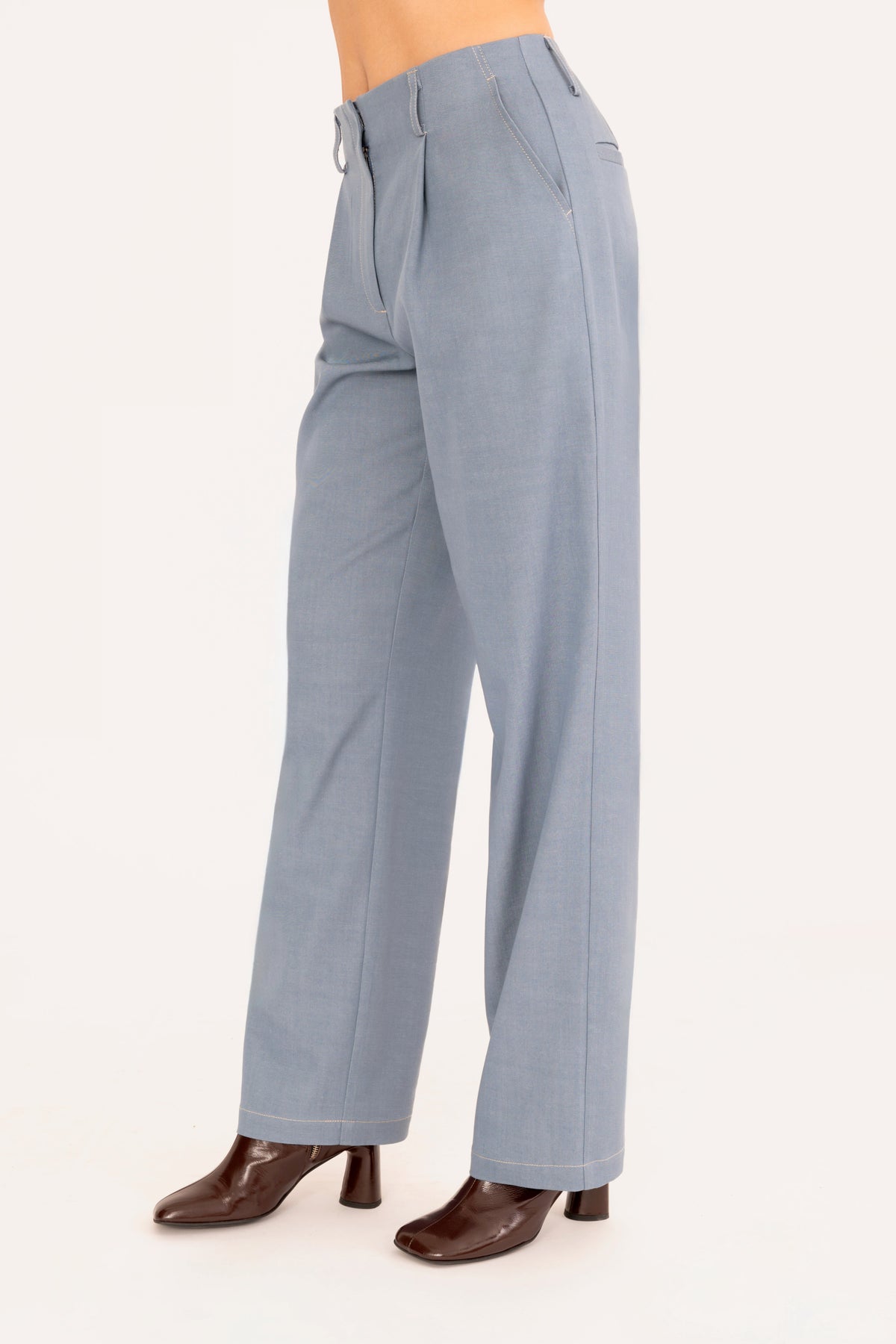 A model is shown from the waist down wearing a pair of light blue denim trousers and dark brown heeled boots against a plain off-white background.