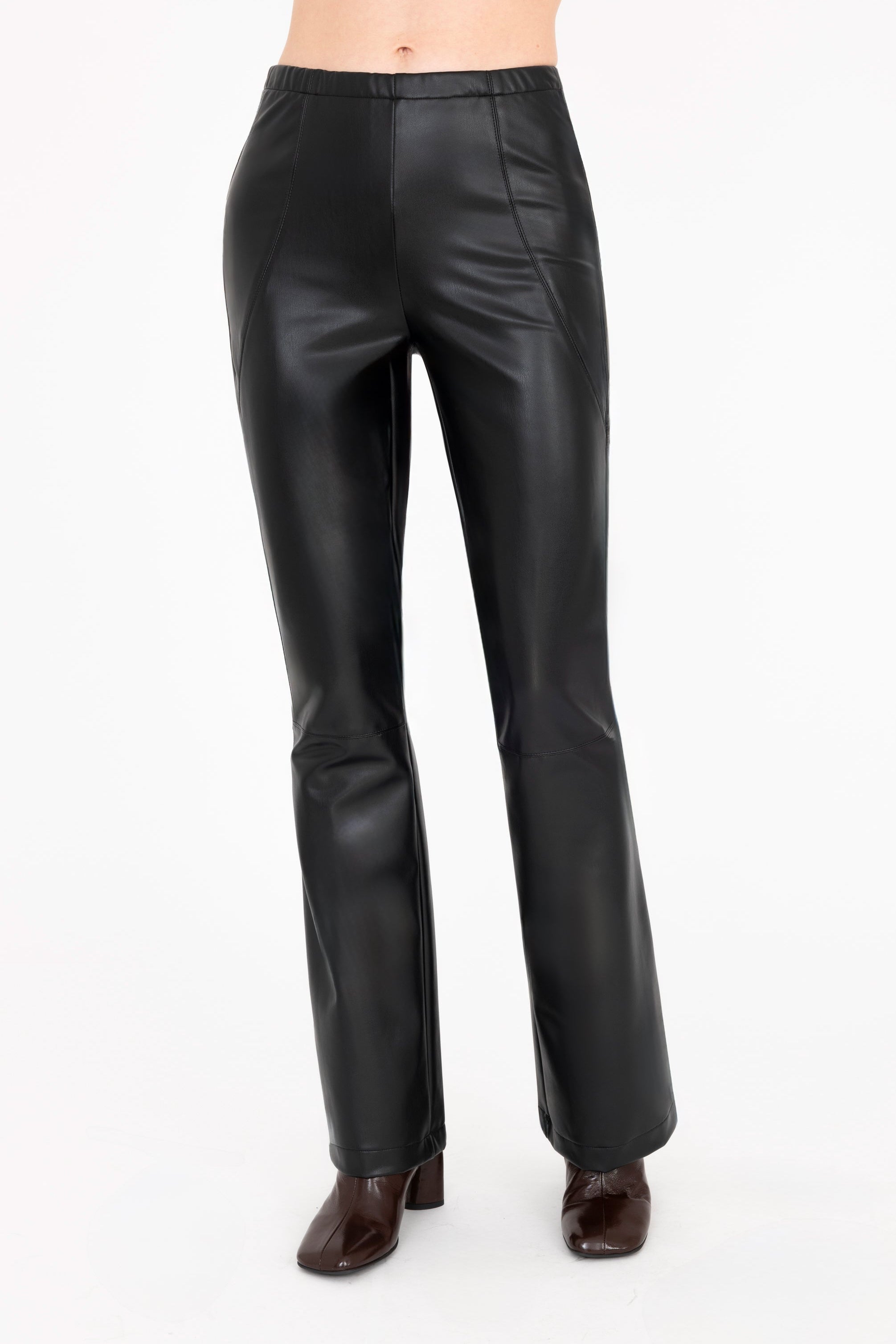 A model is shown from the waist down wearing high-waisted, wide-leg black faux-leather pants and dark brown heeled boots against a plain off-white background.
