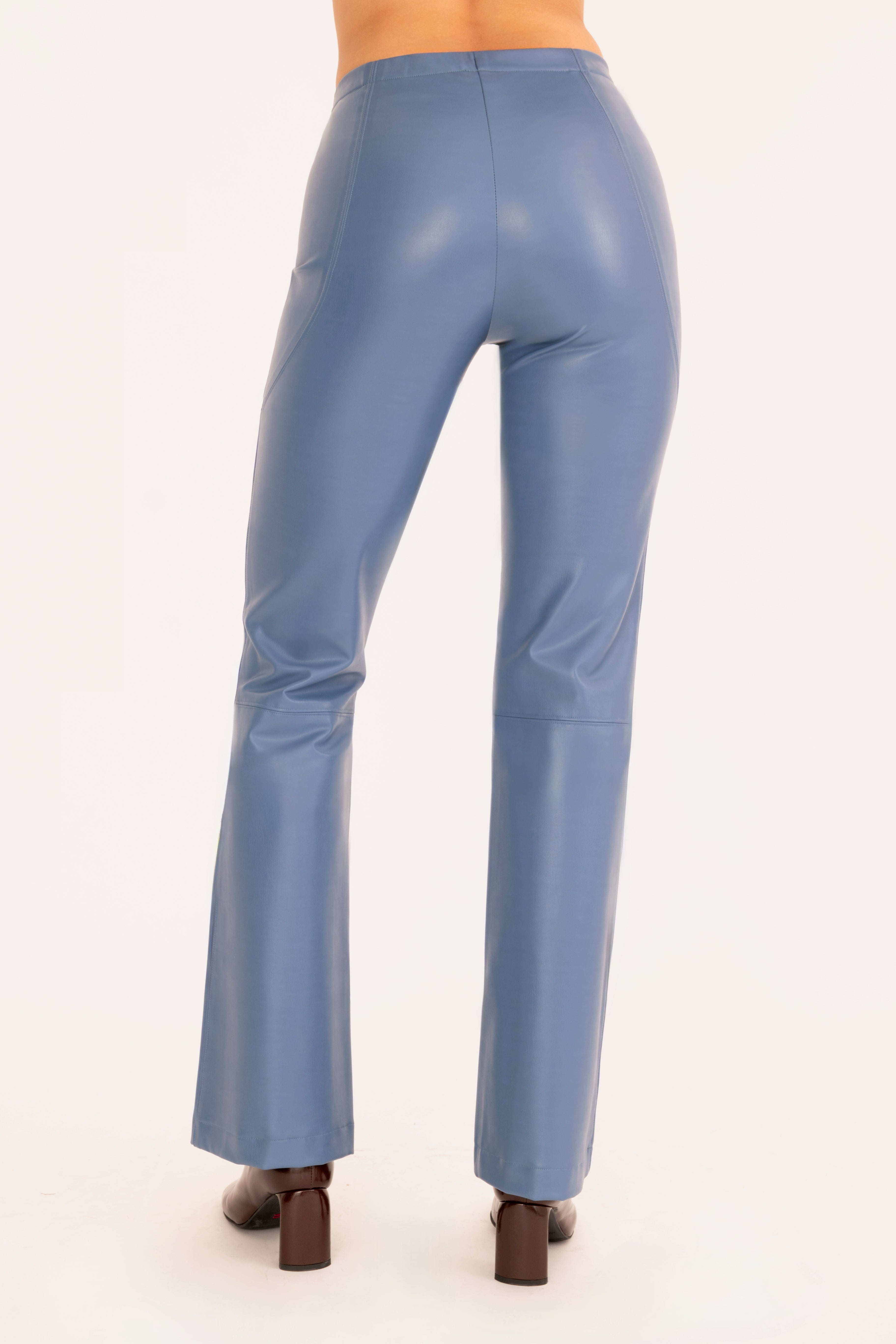 Back view of a model shown from the waist down wearing high-waisted, wide-leg blue faux-leather pants and dark brown heeled boots against a plain off-white background.