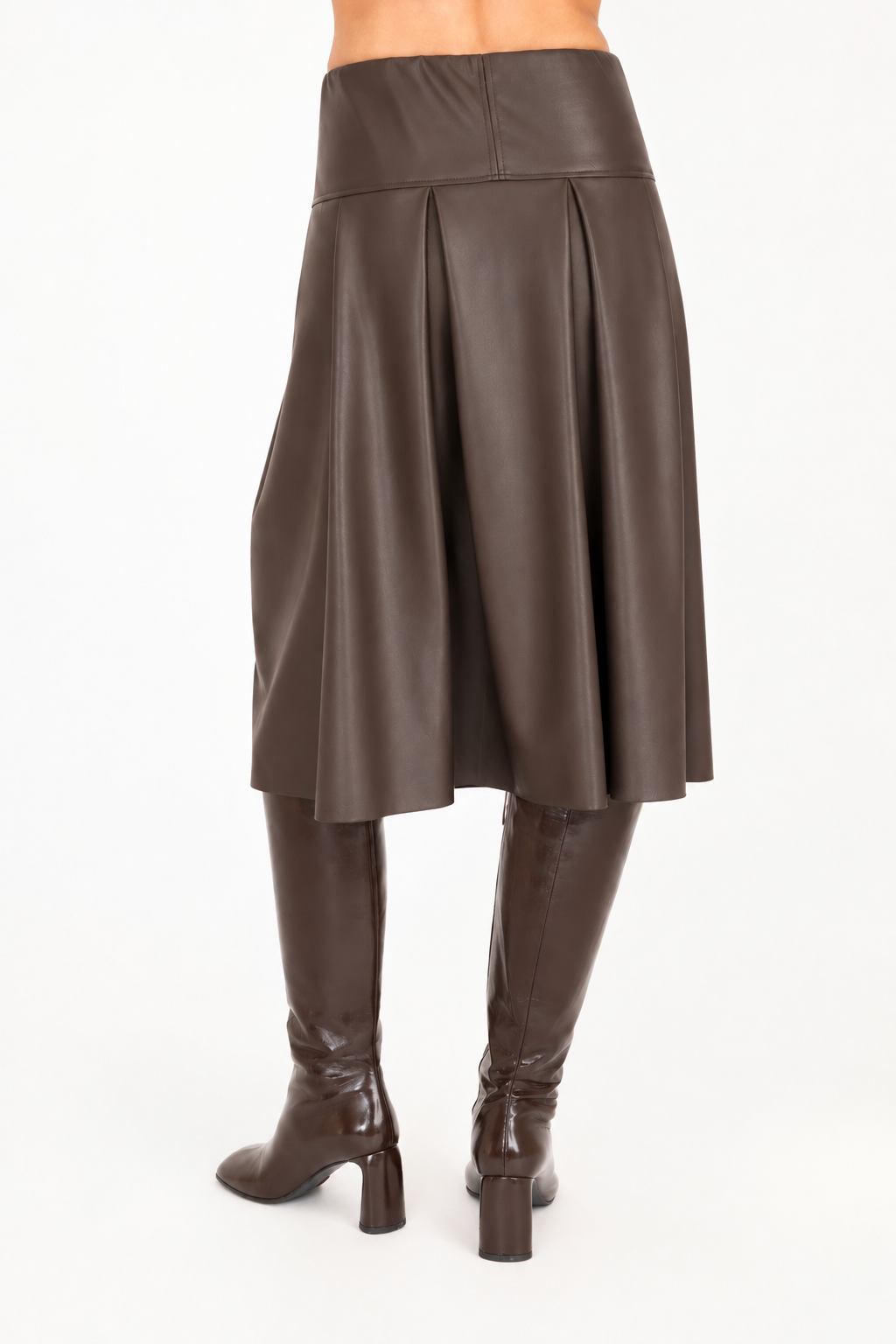Back view of a brown vegan leather pleated A-line skirt shown on a model from the waist down, paired with dark brown knee-high leather boots against a plain white background.