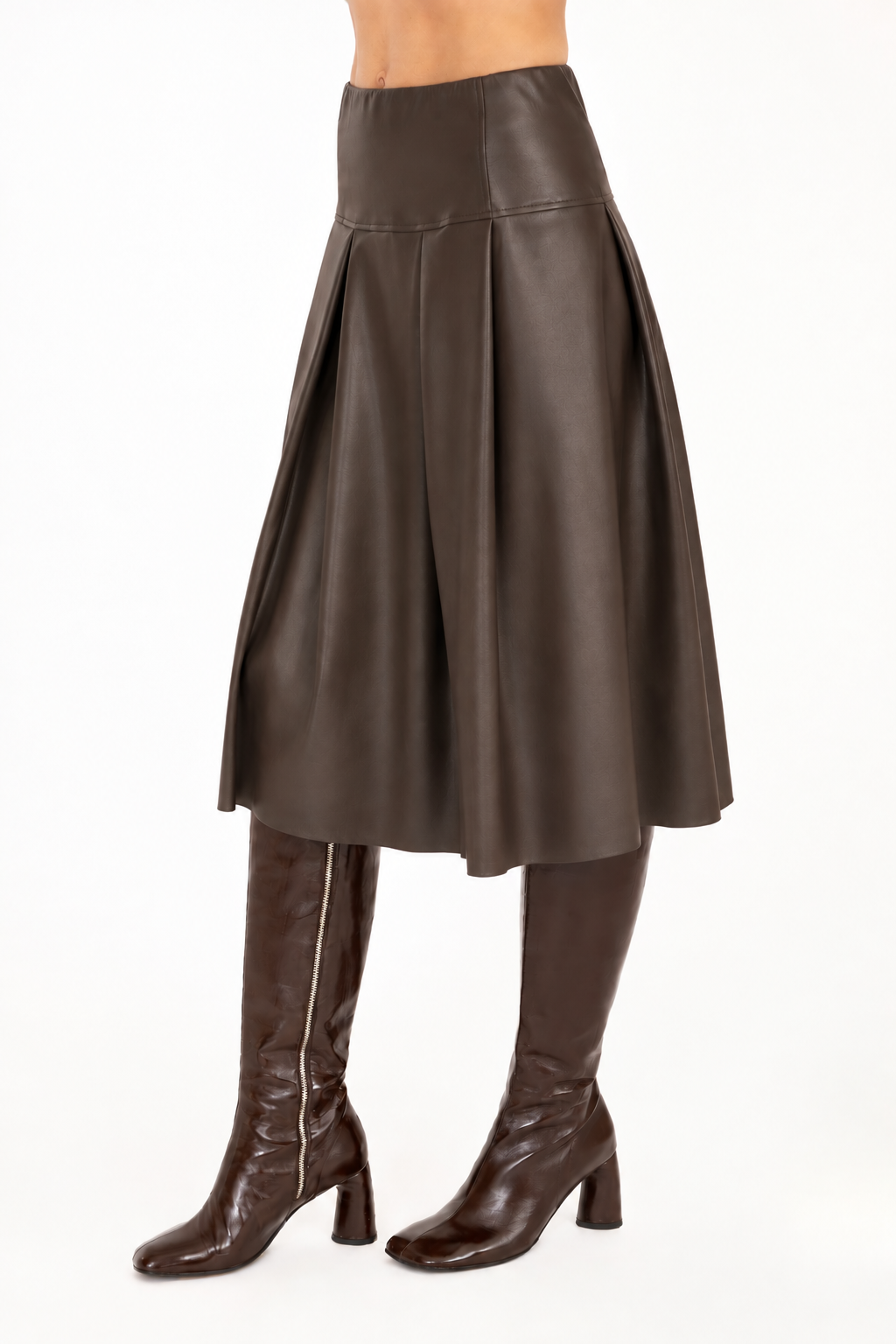 A brown vegan leather pleated A-line skirt shown on a model from the waist down, paired with dark brown knee-high leather boots against a plain white background.