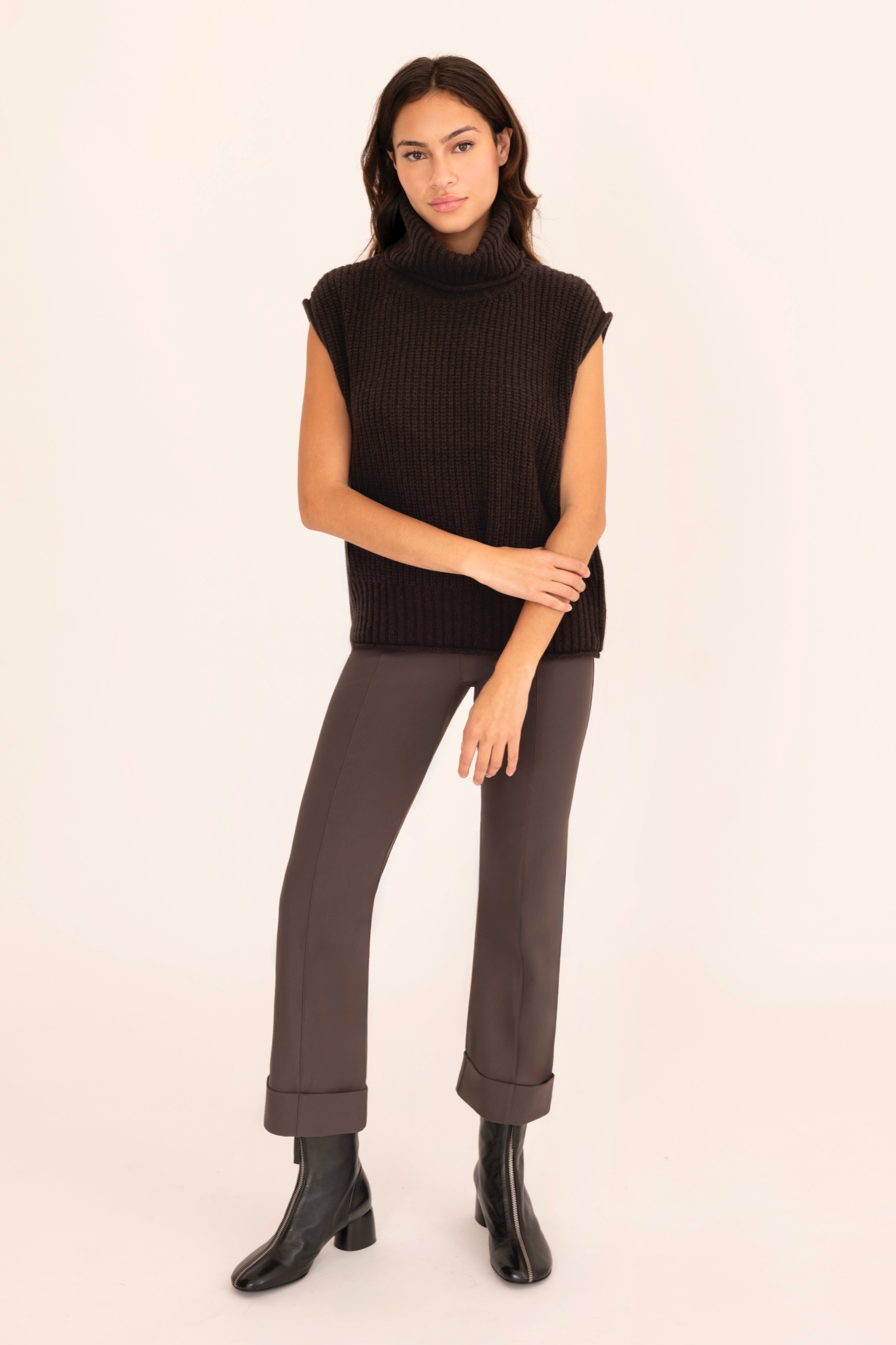 Woman wearing a brown sleeveless sweater and pants on a beige background