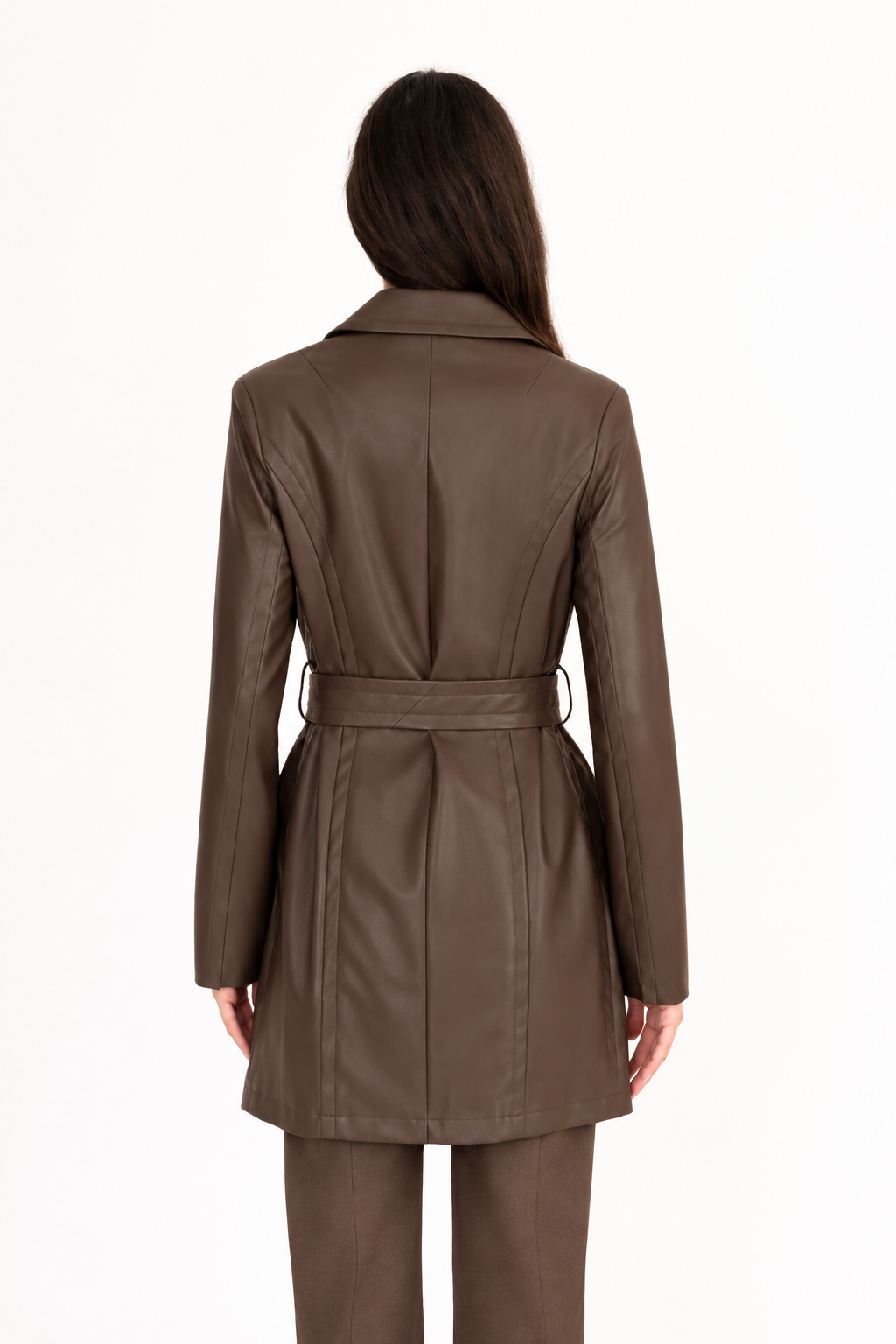 A woman viewed from the back modeling a dark brown vegan leather trench coat with a collar, waist tie, and front pockets, paired with matching dark brown pants, against a plain white studio background.