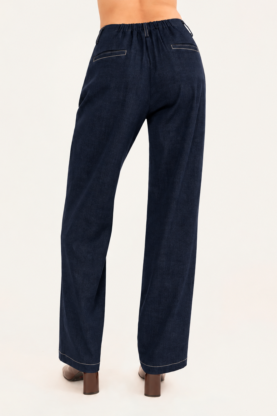 A model shown from the back wearing dark cobalt blue wide-leg denim trousers with brown heeled boots, shown from the waist down against a plain light background.