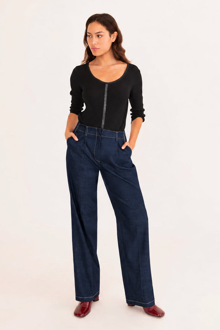 A woman modeling a black ribbed knit top and dark cobalt blue trousers, standing against a plain white studio background.
