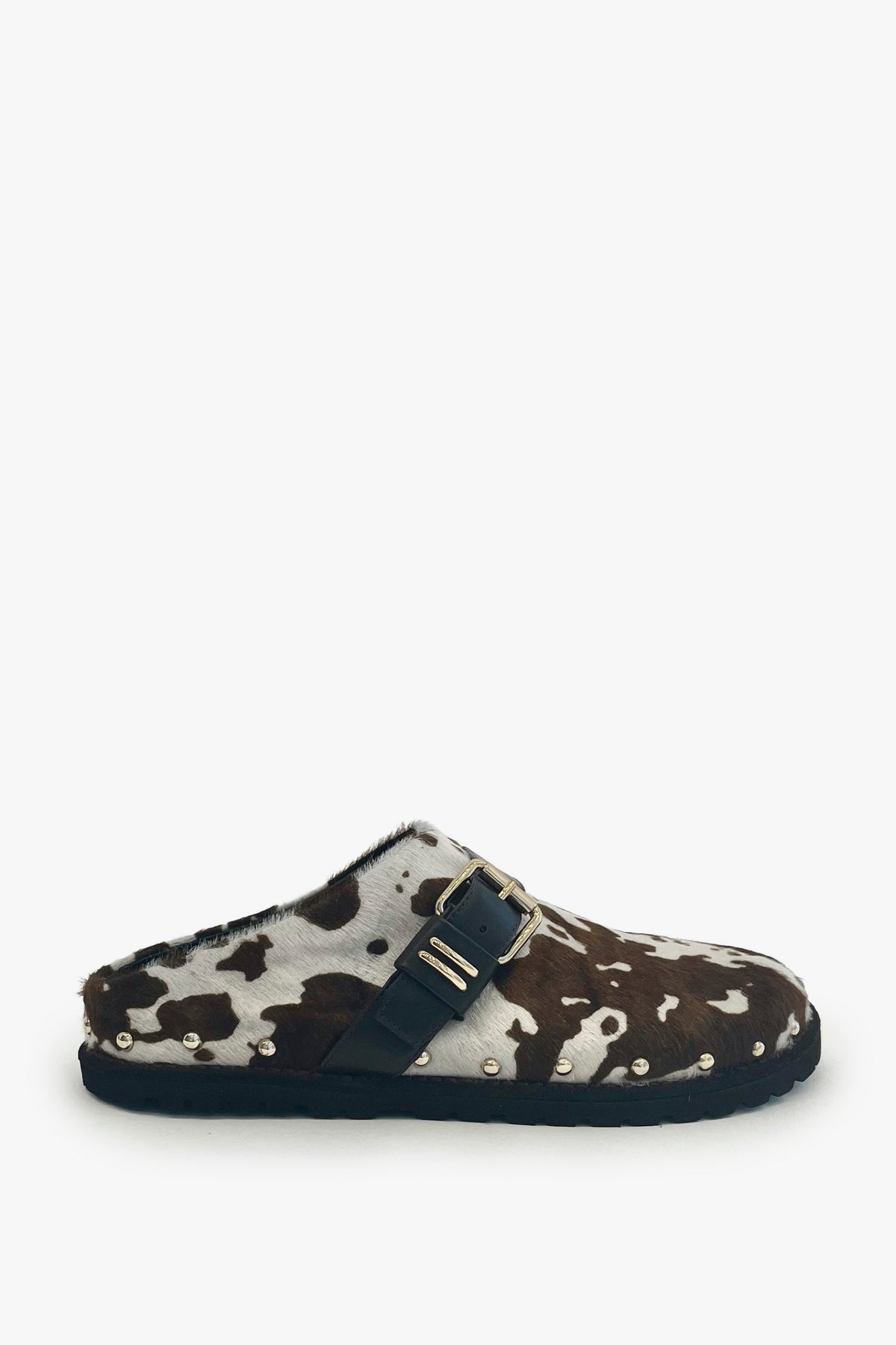 A single slip-on clog-style shoe with a brown and white cow-print upper, a dark navy strap across the top, and a dark sole, shown against a plain light gray background.