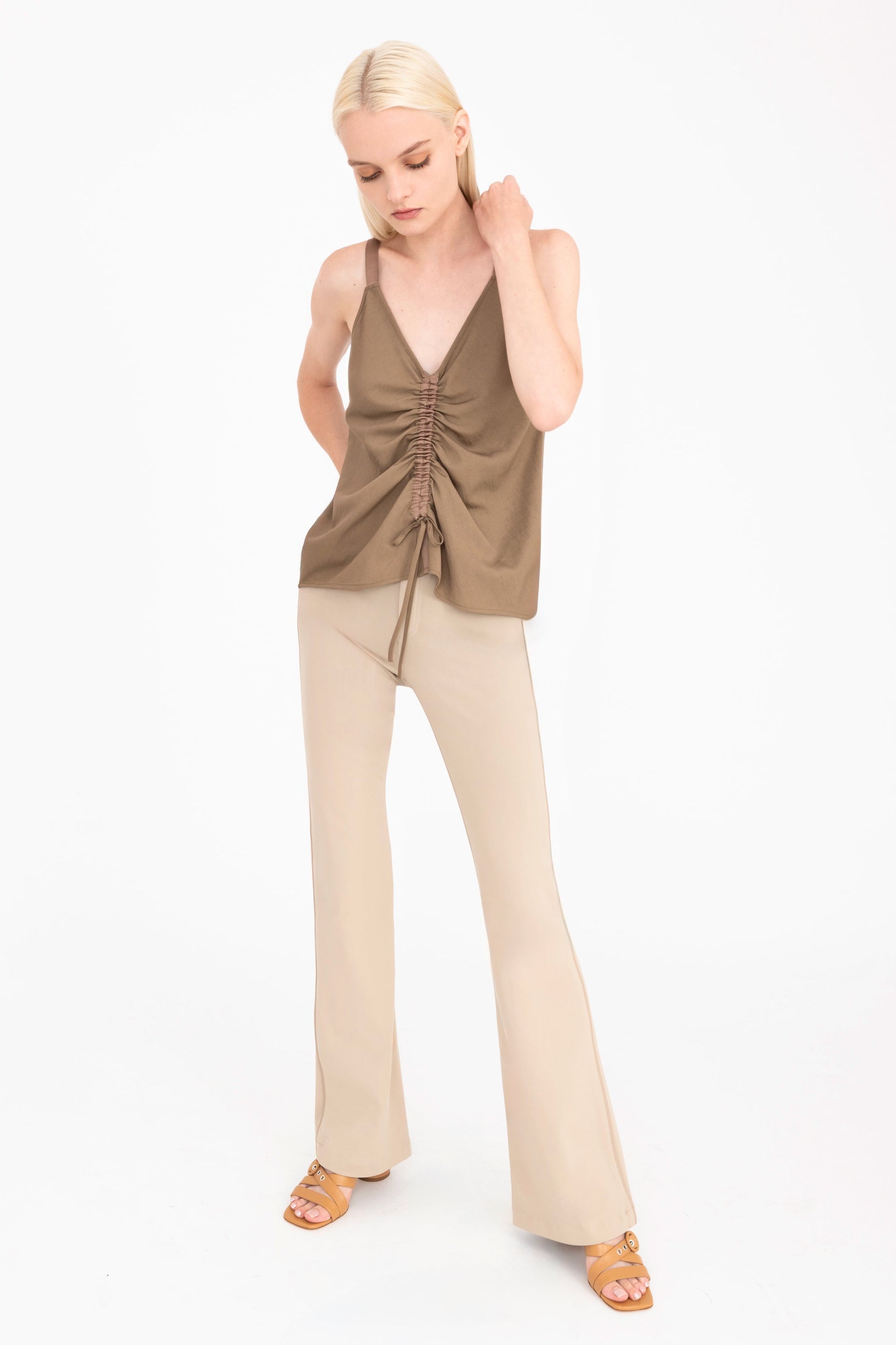 Woman wearing a beige sleeveless top and pants on a white background
