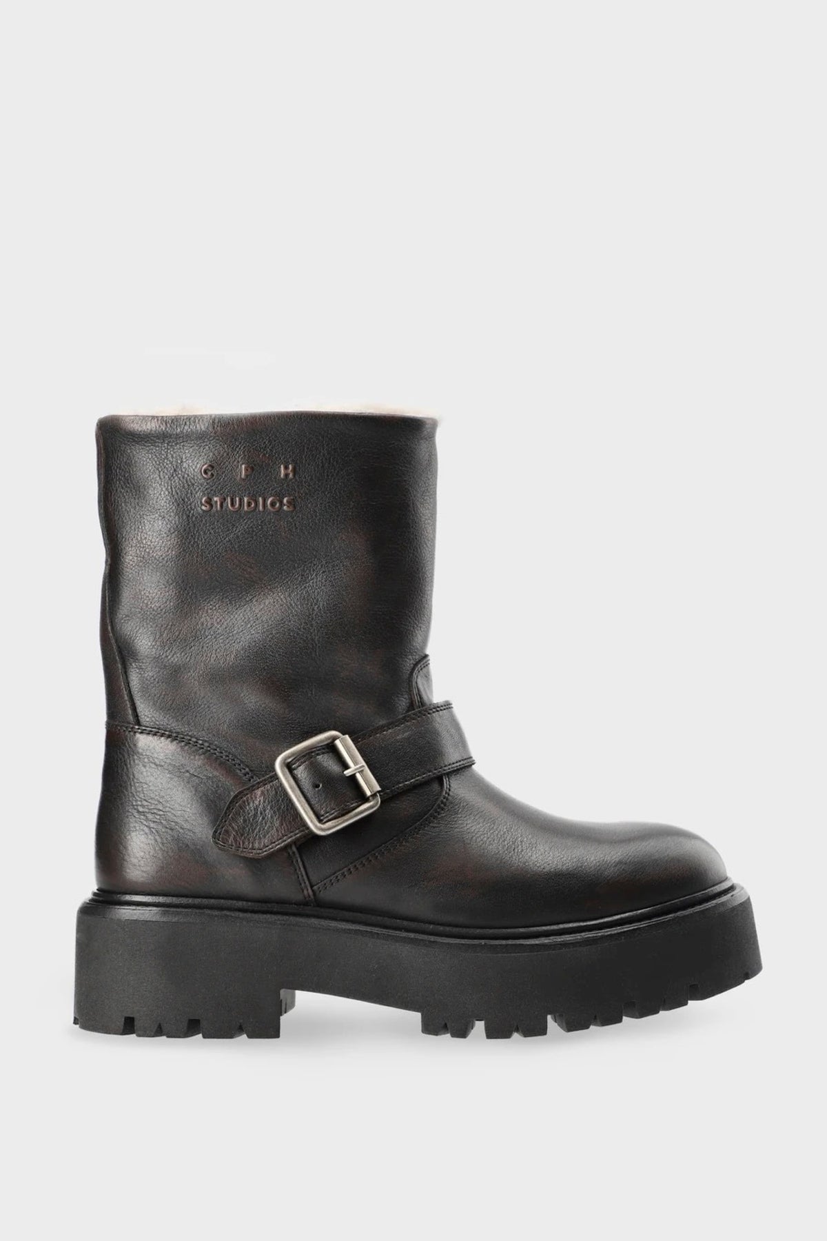 A dark brown leather ankle boot with a chunky lug sole and a wide strap across the instep featuring a silver buckle, shown against a light gray background.