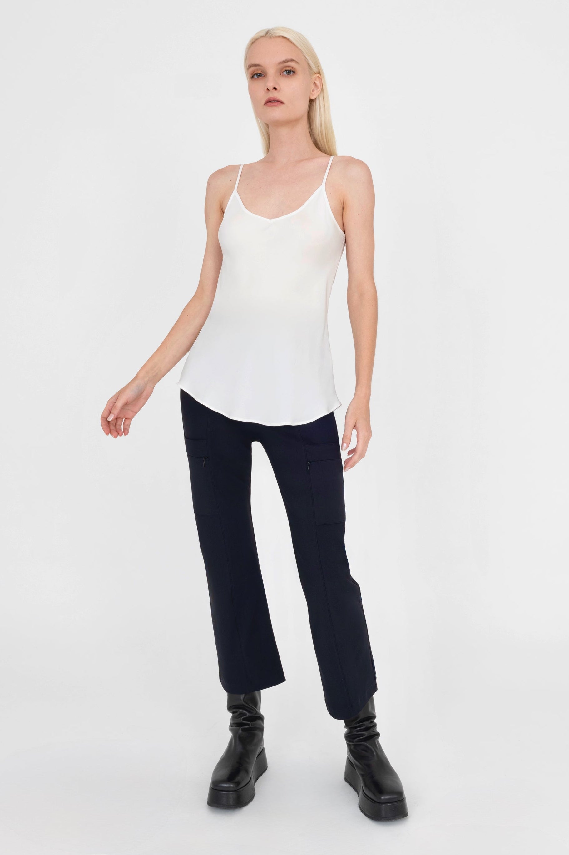 Woman wearing a white tank top and black pants on a white background