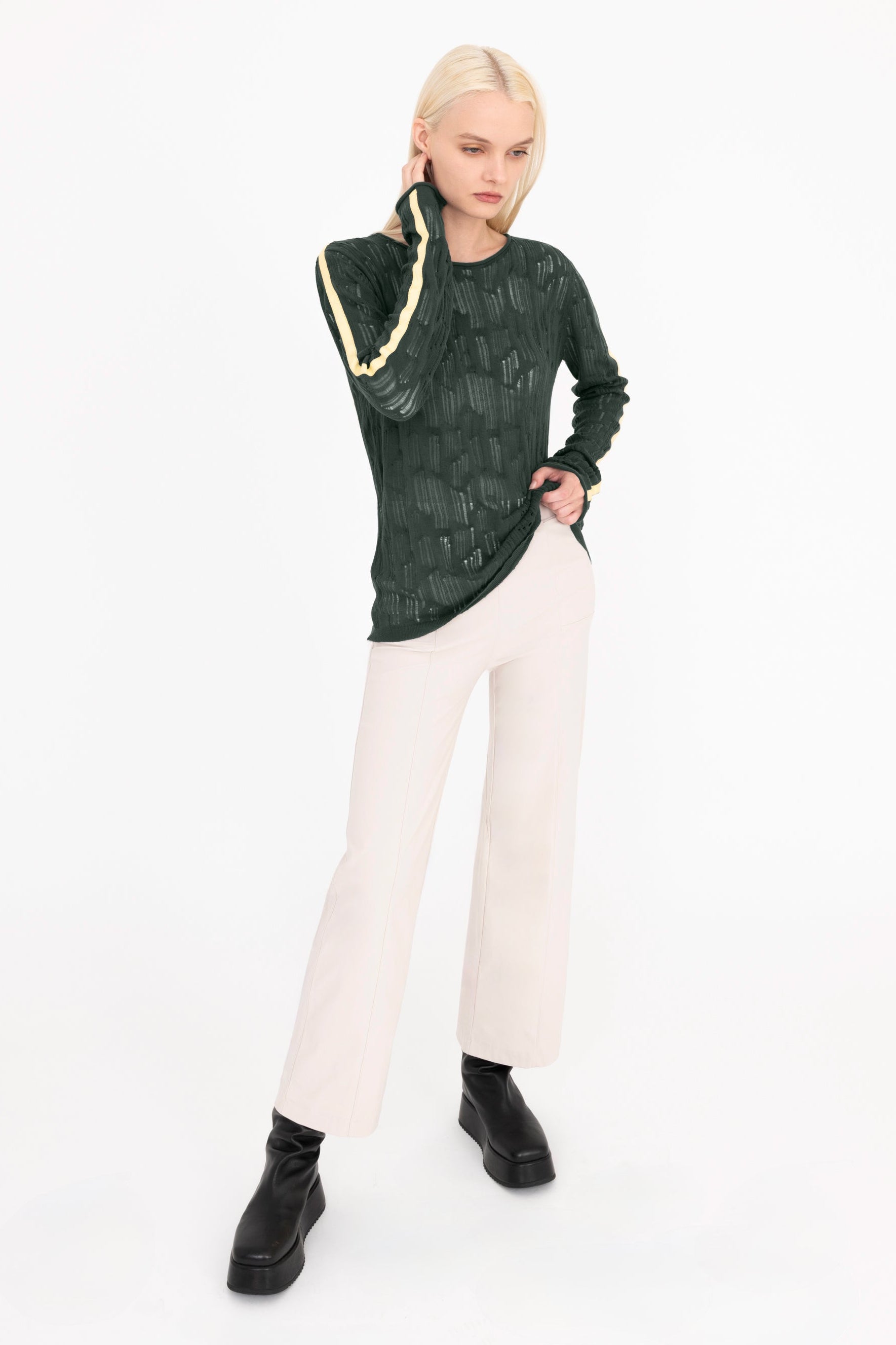 Woman wearing a green sheer top with cream stripes and beige pants on a white background