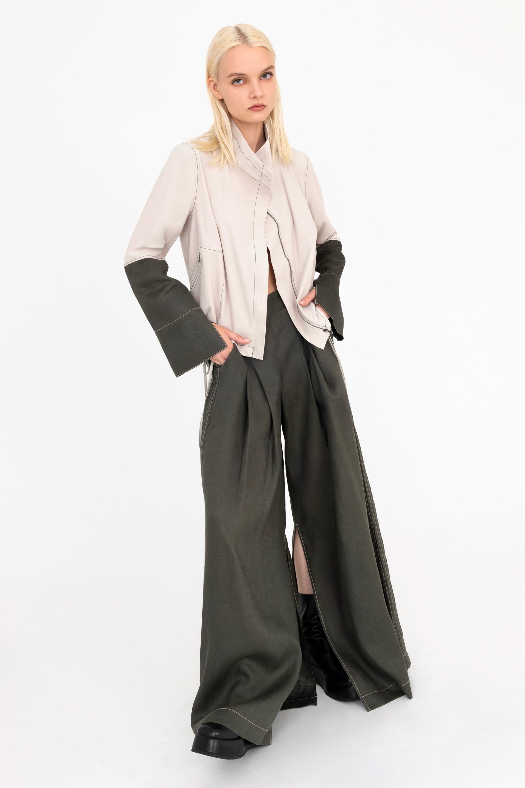 Woman wearing a beige jacket and pine green pants with a white background