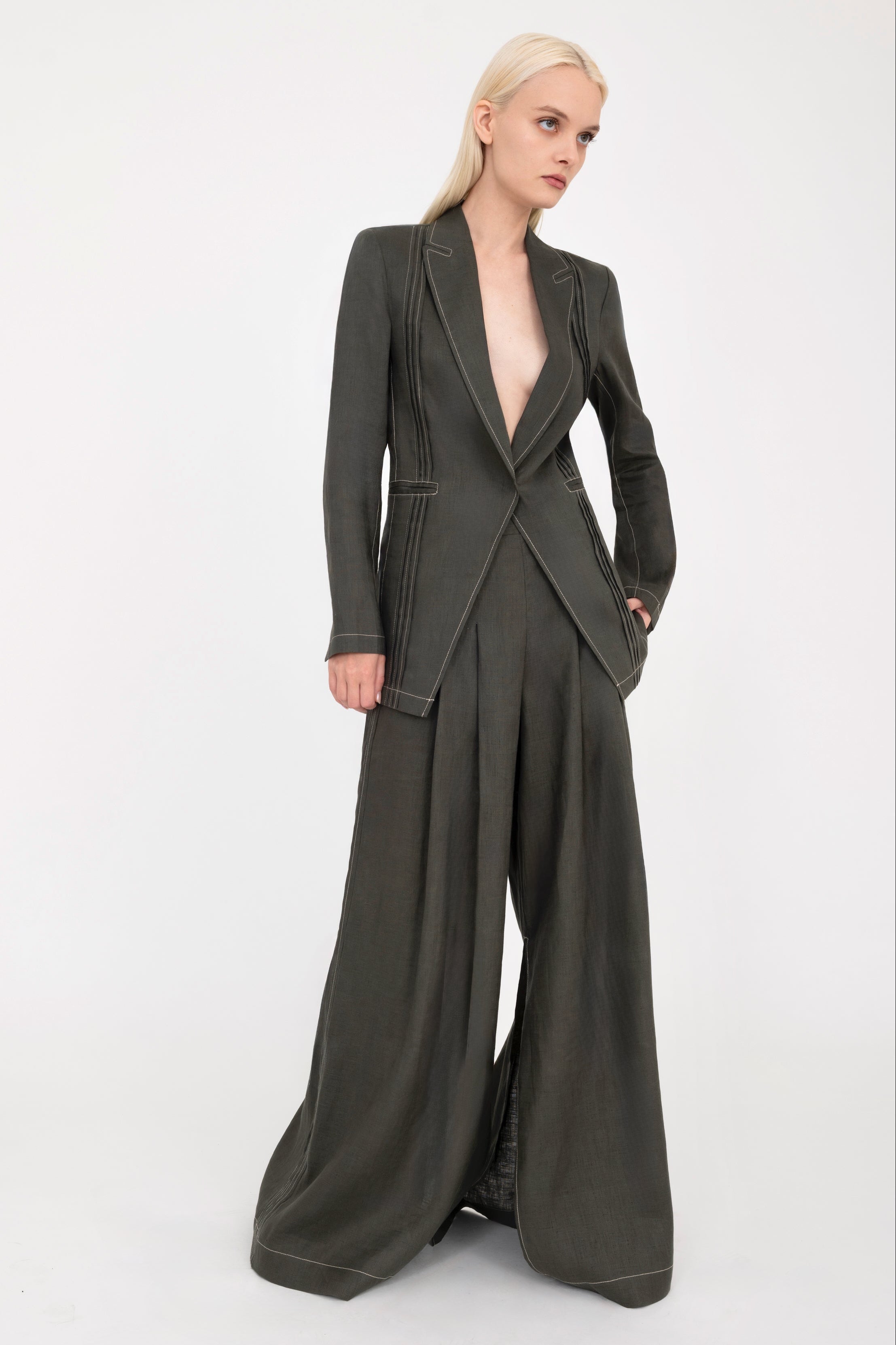 Woman wearing a pine green blazer and wide-leg pants with a white background
