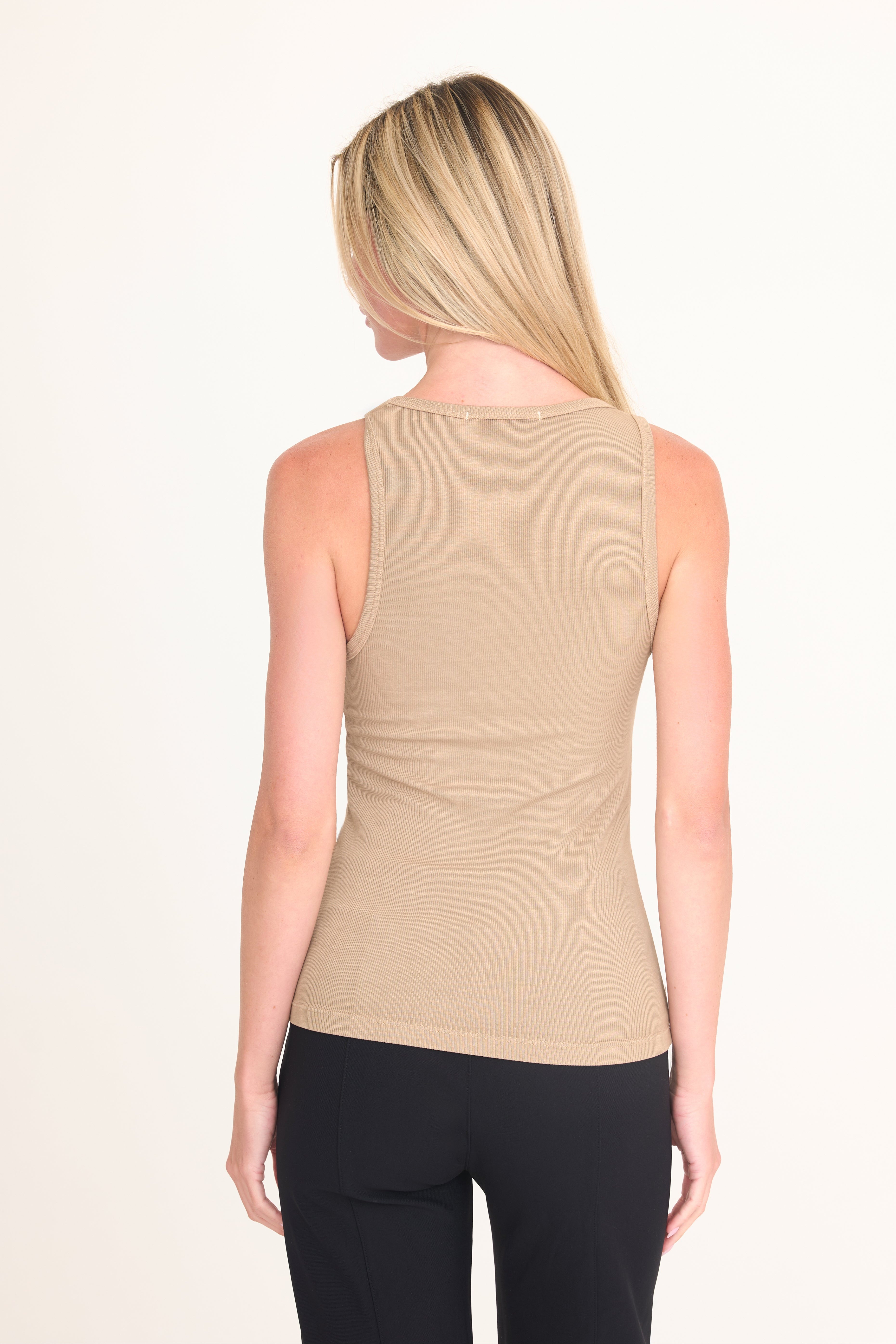 A woman viewed from the back wearing a fitted sleeveless ribbed tank top in light beige and black pants, against a plain light background.