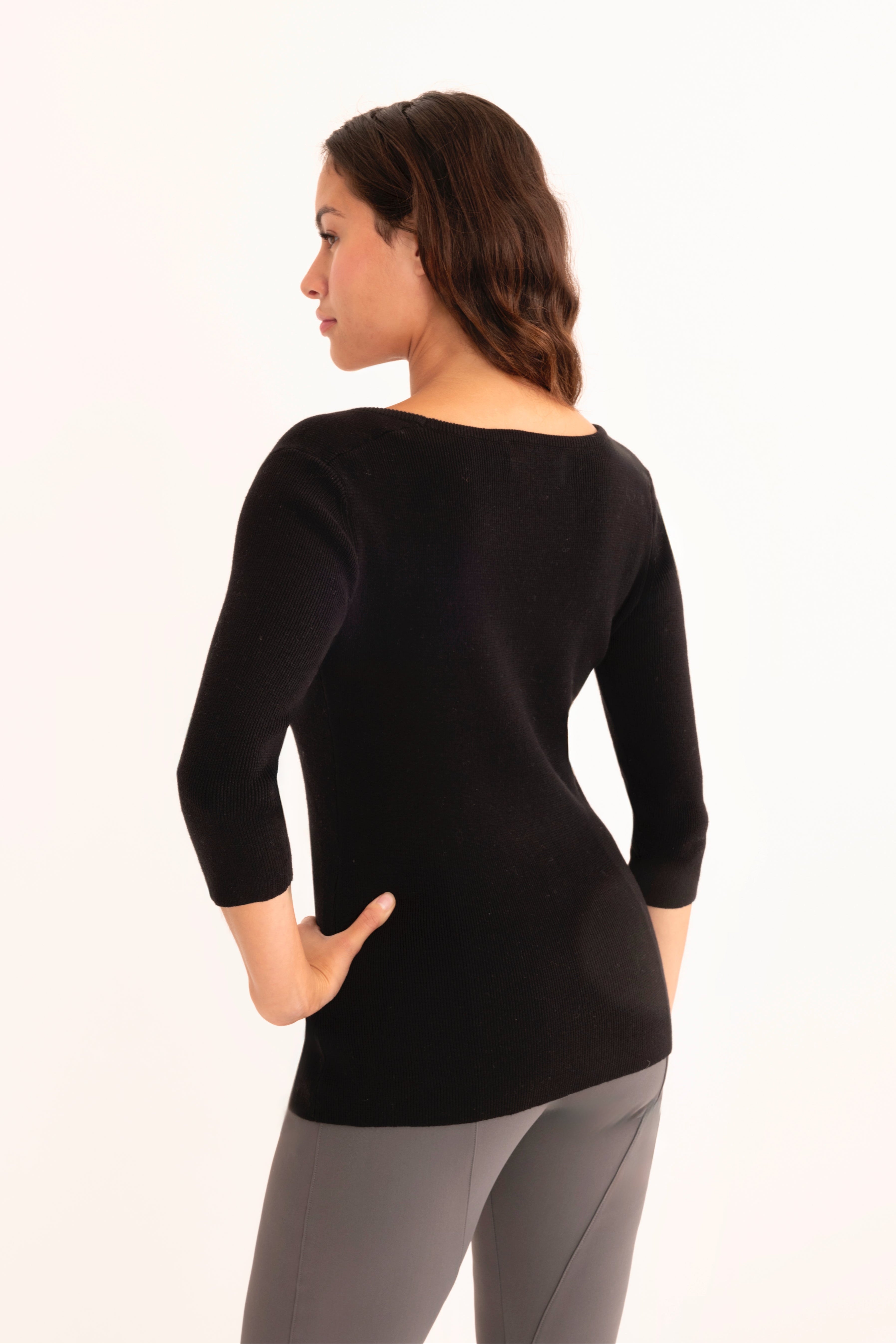Back view of woman wearing a black top and gray pants on a white background