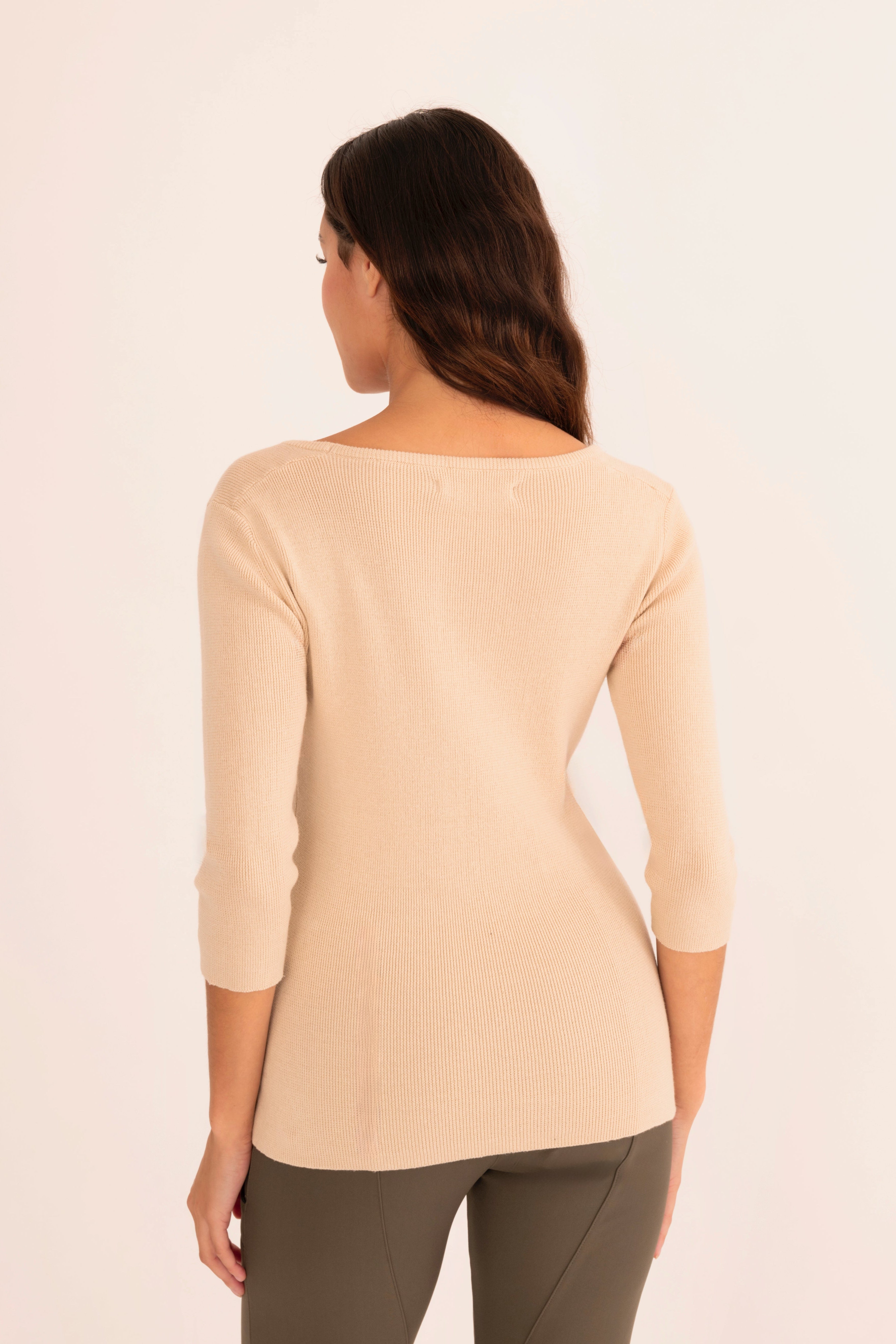 Back view of woman wearing a beige top and green pants on a white background
