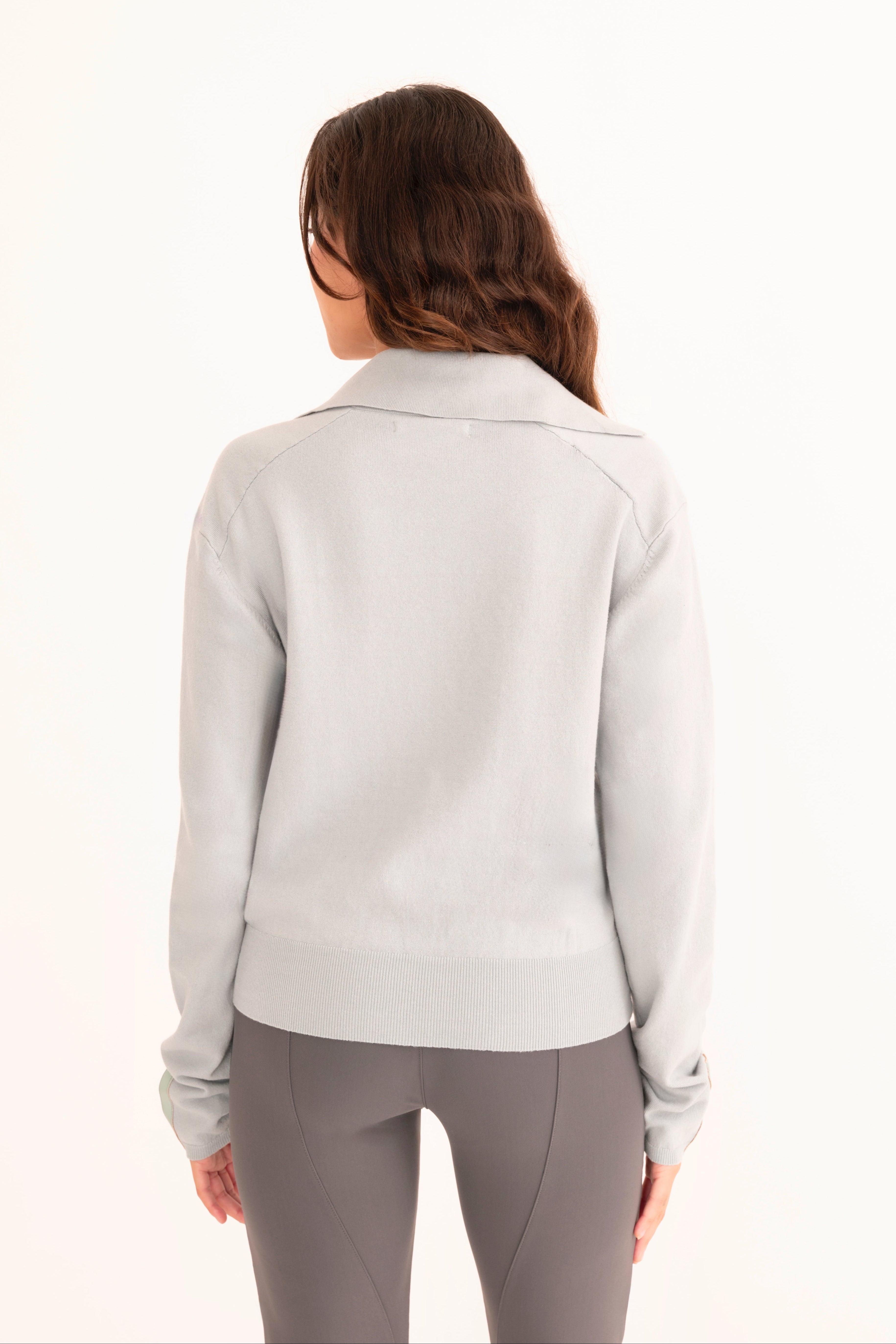 Back view of woman wearing a light blue zip-up jacket and gray pants on a white background