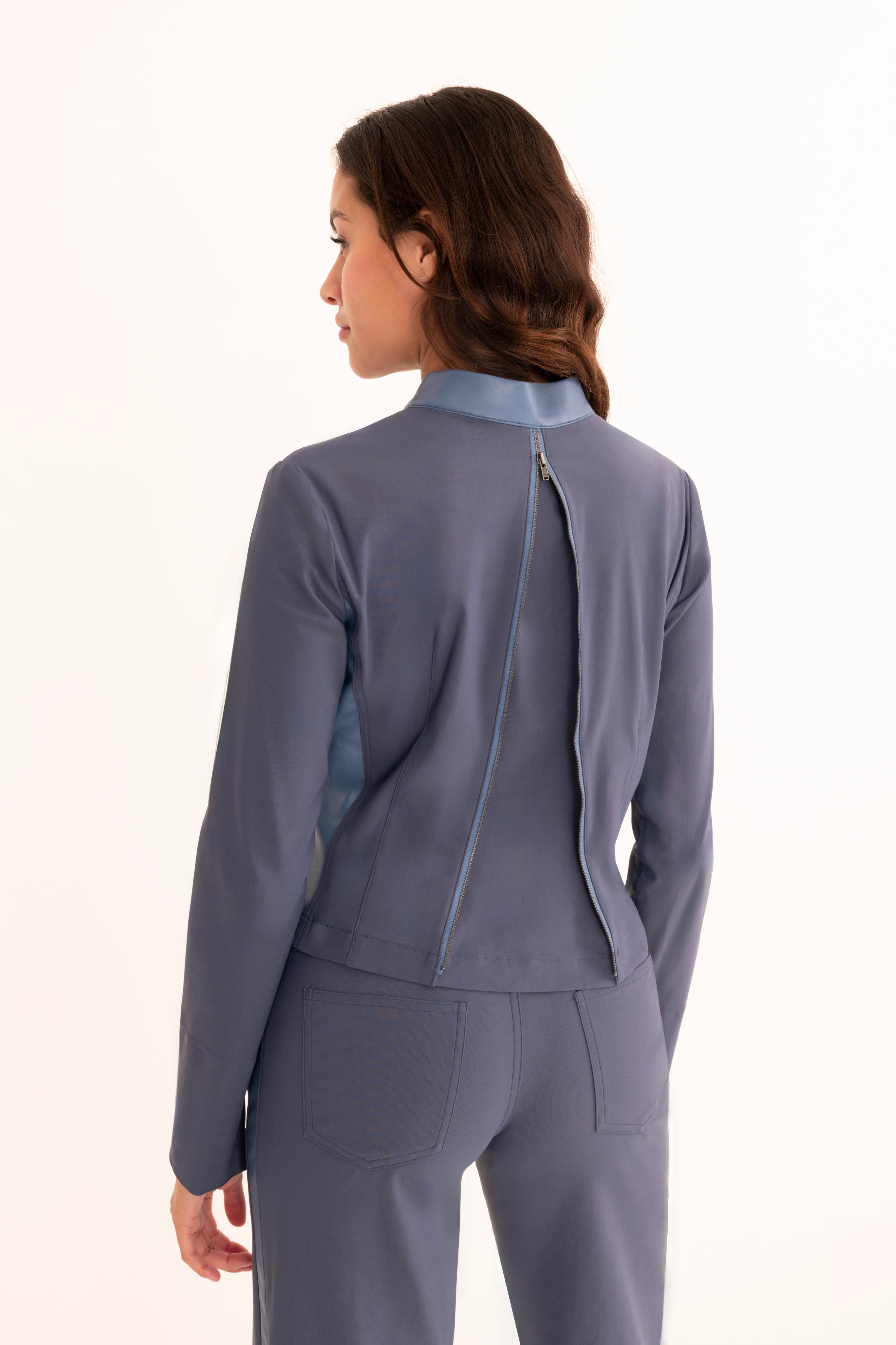 A woman shown from the back wearing a tailored blue-gray jacket and matching trousers against a plain white studio background.