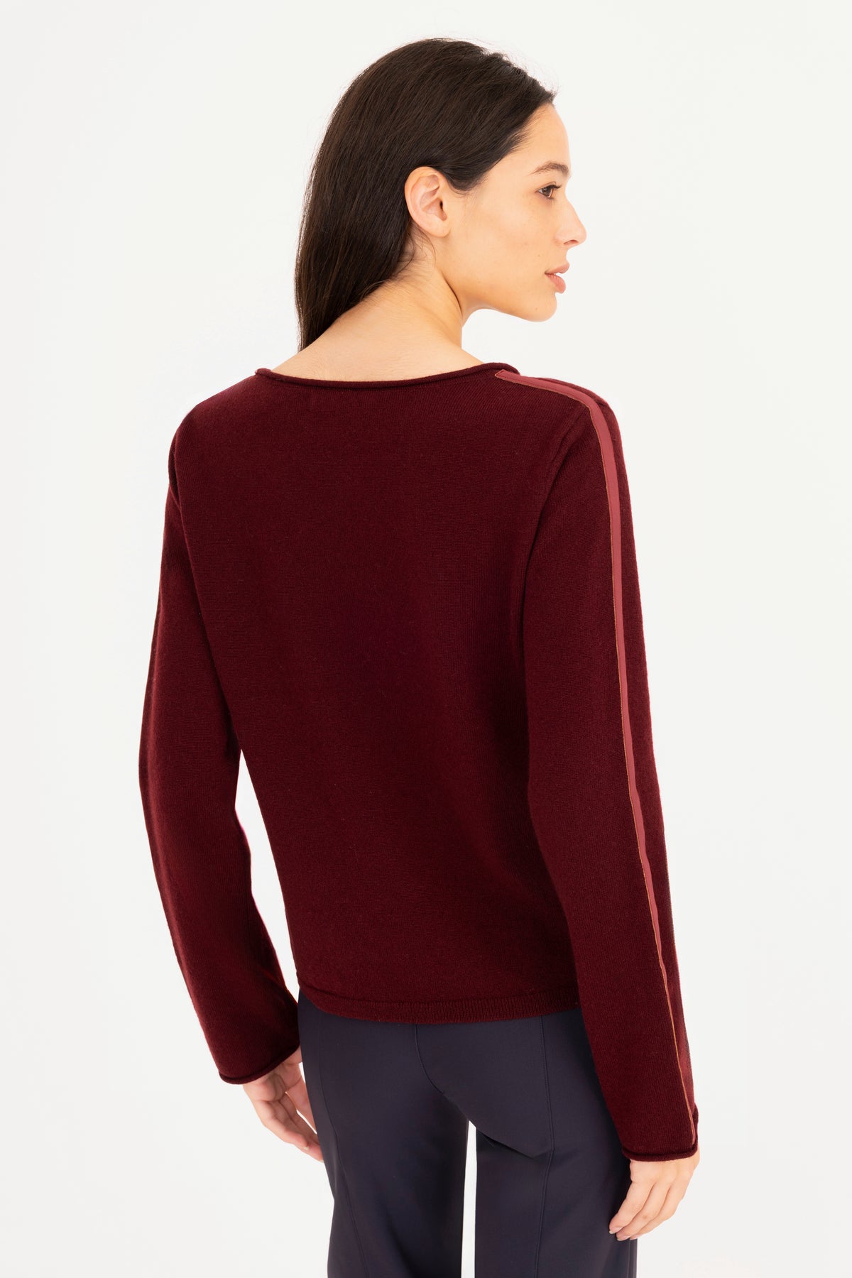 A woman shown from the back wearing a long-sleeve knit sweater in burgundy, paired with dark navy pants, against a plain white studio background.